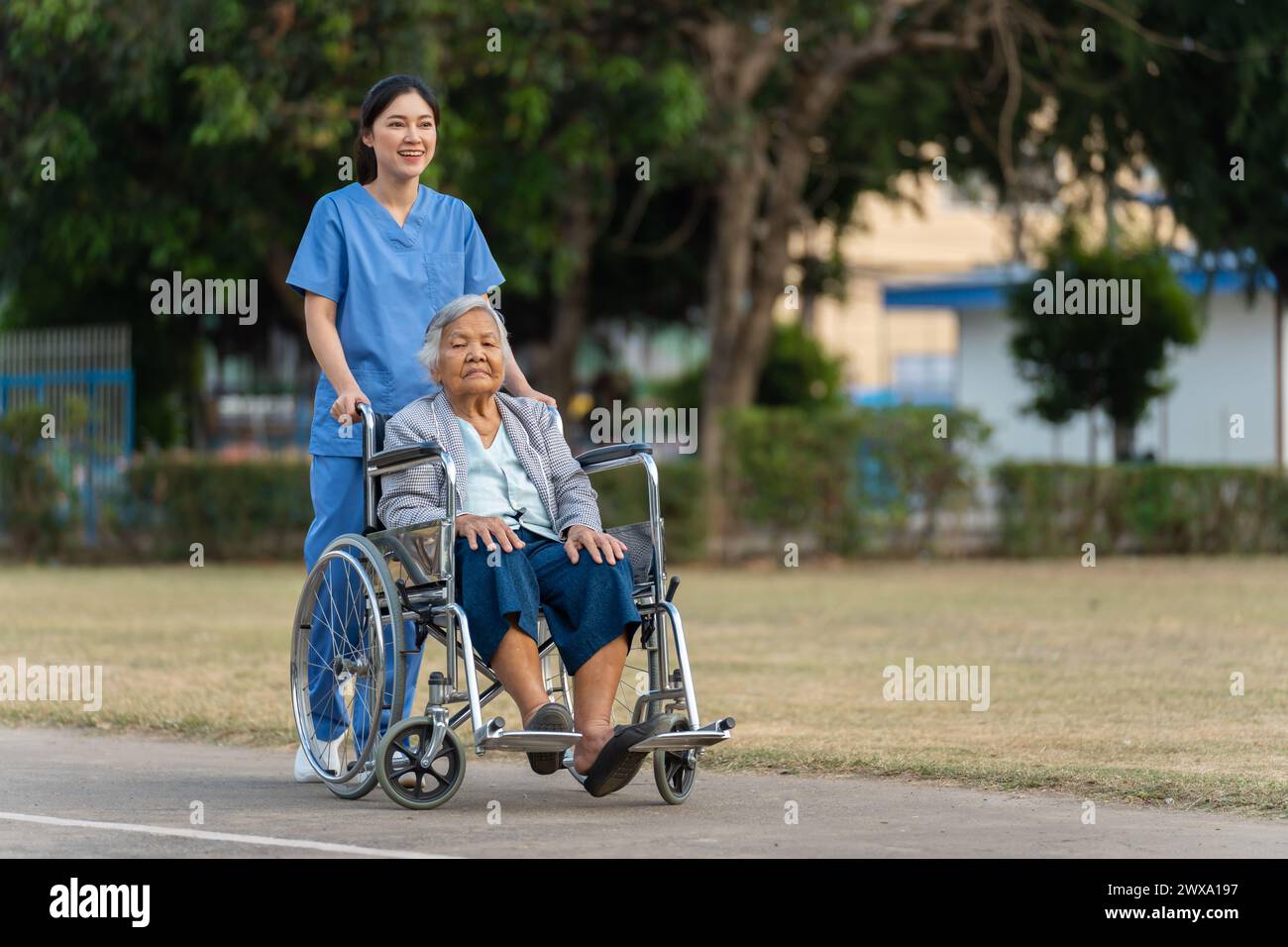 Glückliche Krankenschwester kümmern sich und schieben Seniorin im Rollstuhl im Park, freundliche Betreuerin Stockfoto