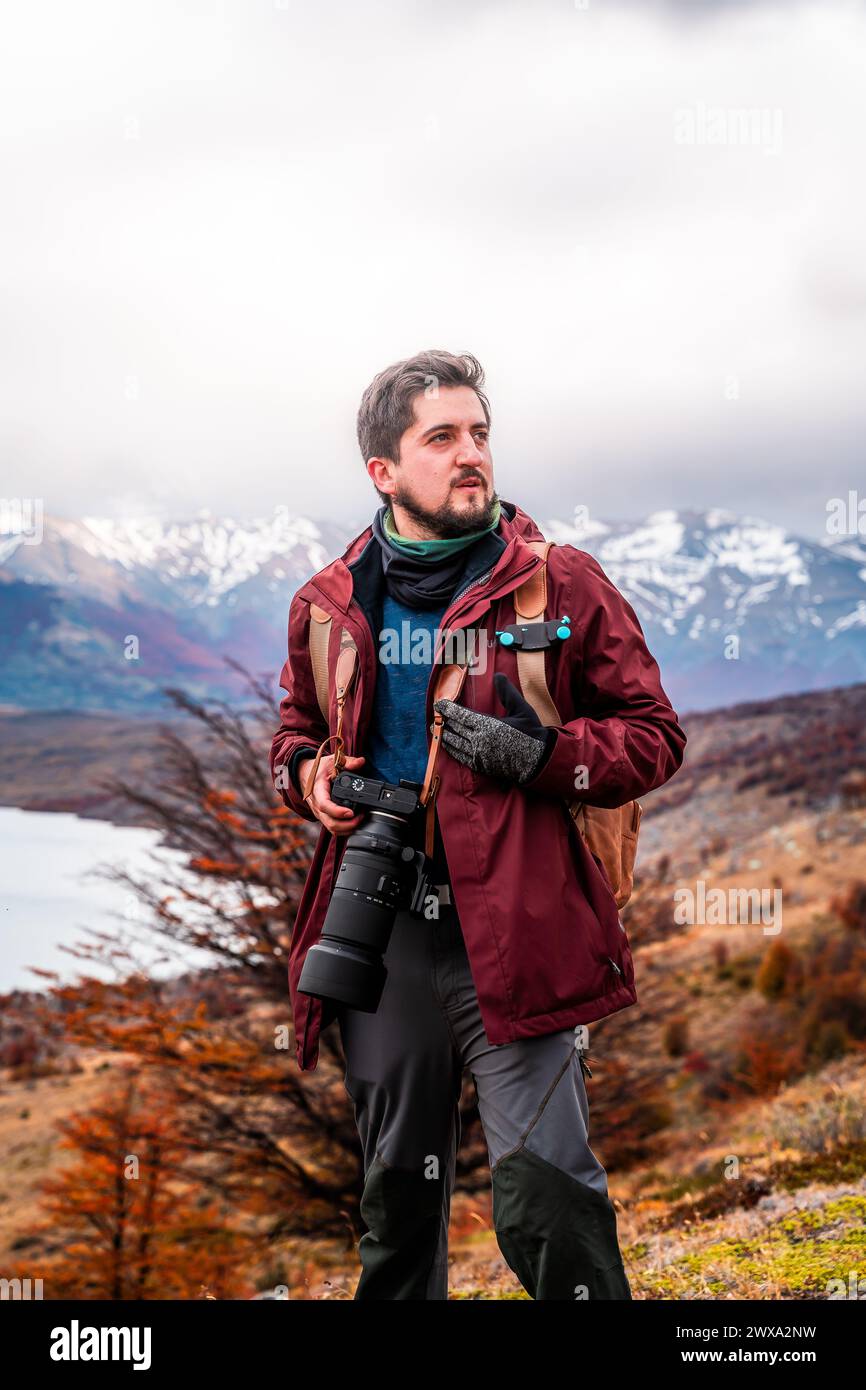 Eine vertikale Aufnahme eines Mannes mit einer Kamera auf einem Berggipfel, umgeben von Bergen Stockfoto