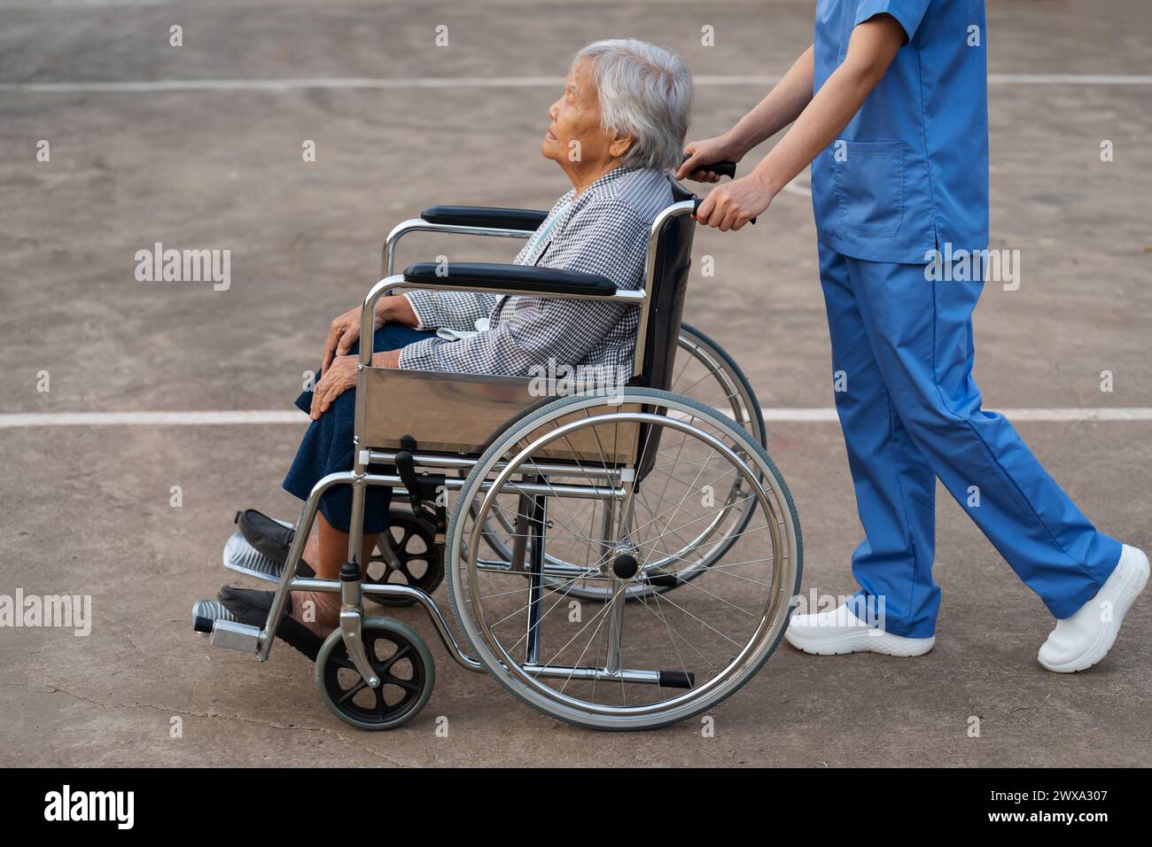 Schwester kümmert euch und schiebt Seniorin im Rollstuhl im Park, freundliche Betreuerin Stockfoto