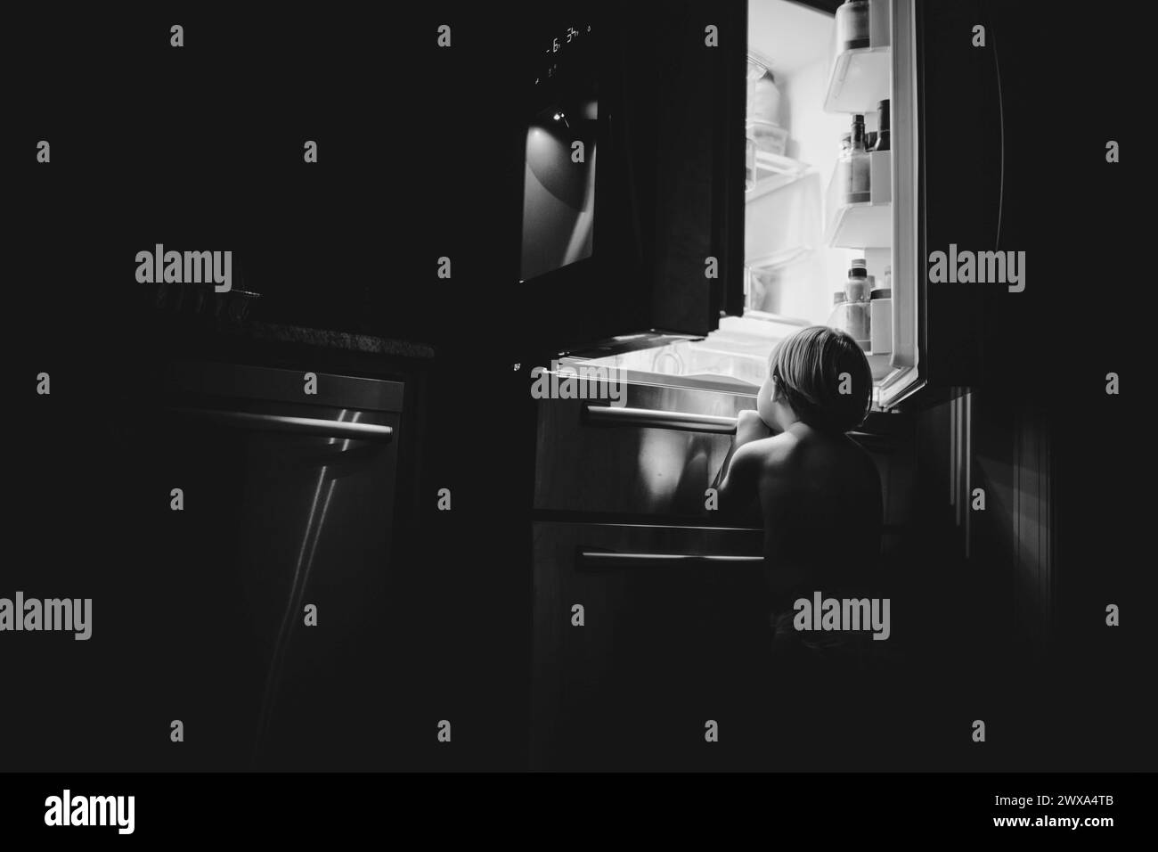Das Kind schaut in das Licht des Kühlschranks in einem ruhigen Zuhause Stockfoto