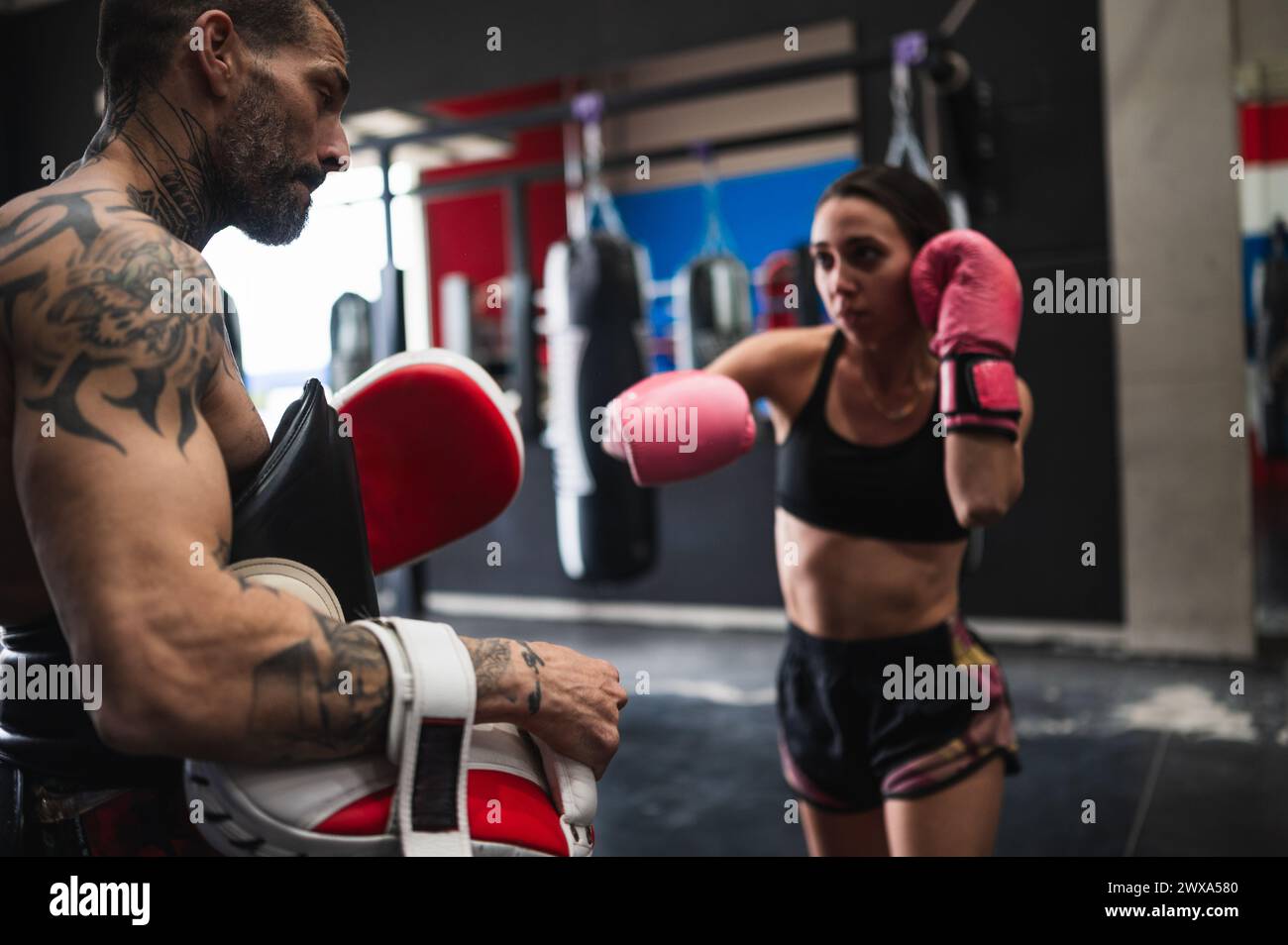 Fokussierter weiblicher Boxer-Sparring mit Personal Trainer im Fitnessstudio Stockfoto