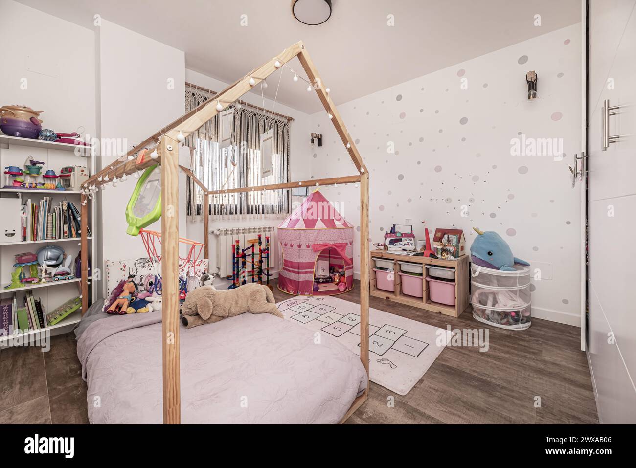 Kinderzimmer mit großem Einbauschrank mit weißen Türen, Regalen voller Bücher und Spielzeug und einem Bett mit unbehandelter Holzstruktur Stockfoto