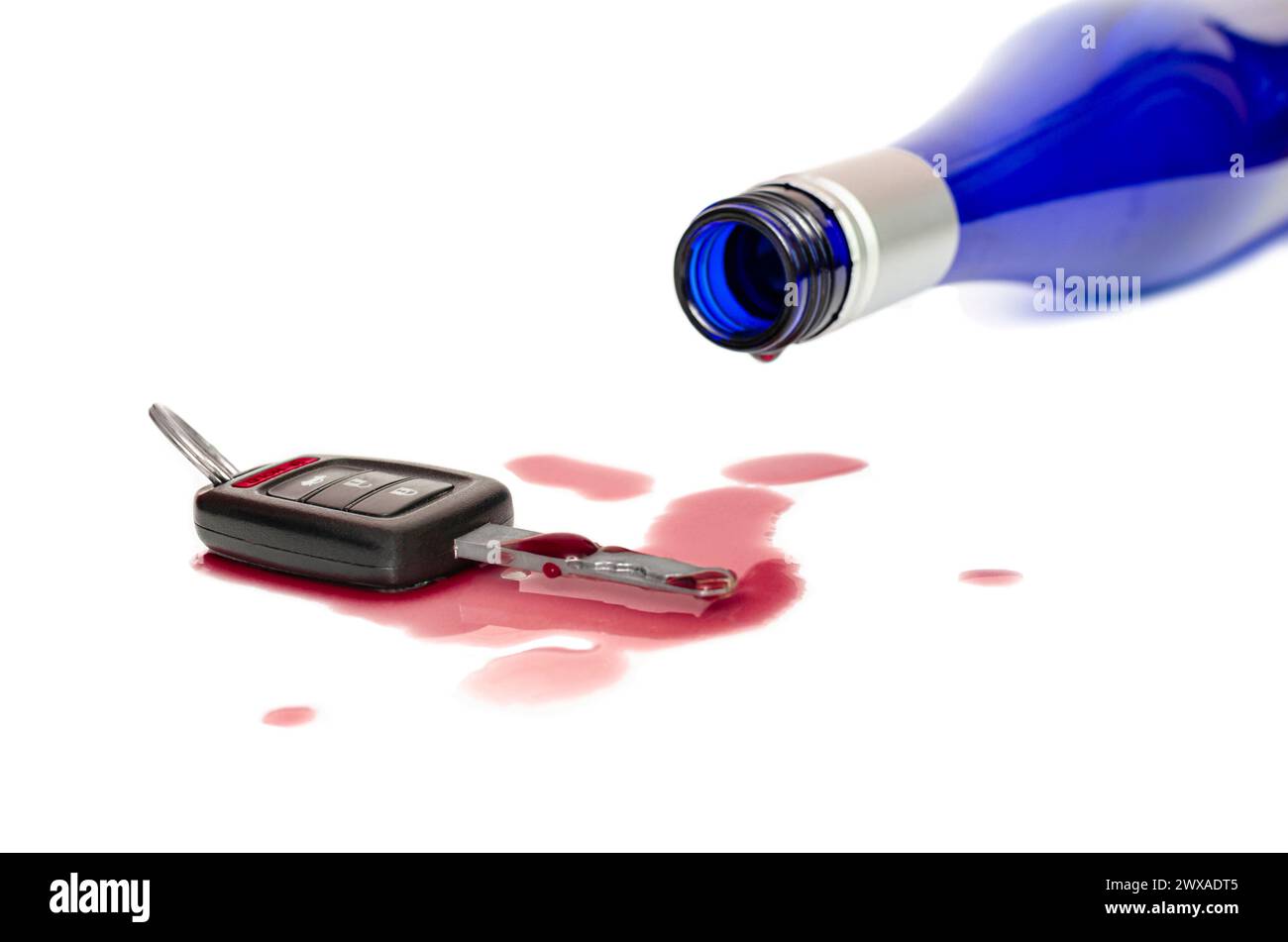 Autoschlüssel auf dem Tisch und verschütteter Wein aus der Flasche, nicht trinken und fahren Konzept, isolierter weißer Hintergrund Stockfoto
