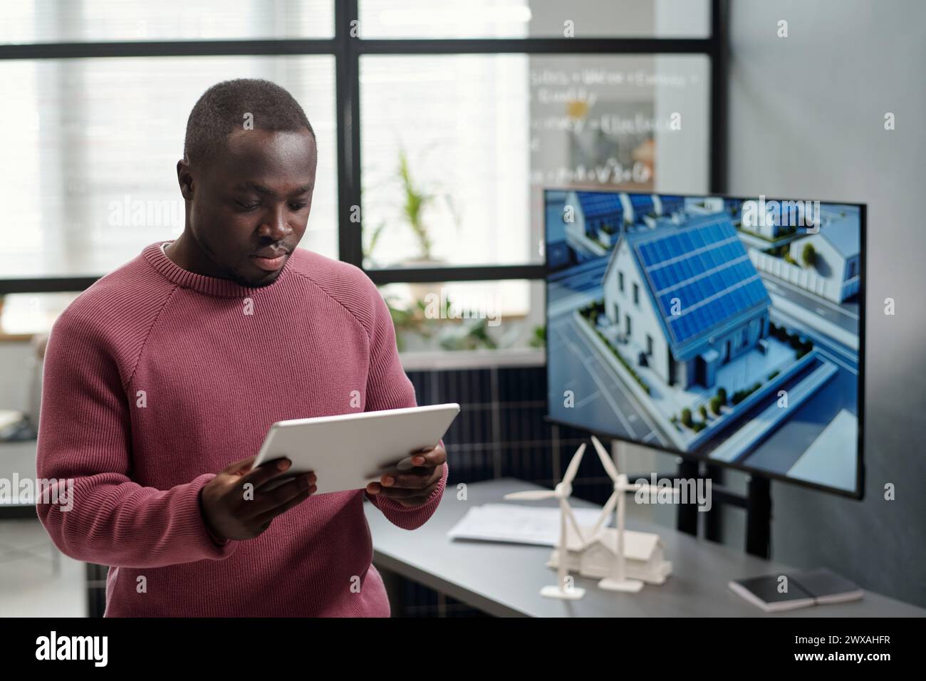 Afroamerikanischer männlicher Mitarbeiter in der Vernetzung von Casualwear oder beim Scrollen durch Projektpunkte an seinem Arbeitsplatz mit interaktivem Board Stockfoto
