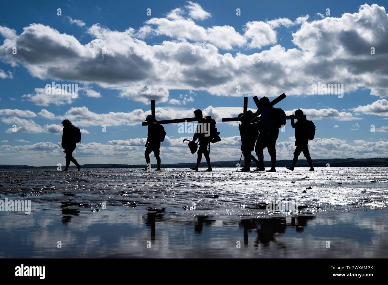 Pilger mit Holzkreuzen über den Sand bei Ebbe zur Heiligen Insel Lindisfarne im Northumberland während der jährlichen christlichen Osterpilgerfahrt am Karfreitag. Bilddatum: Freitag, 29. März 2024. Stockfoto