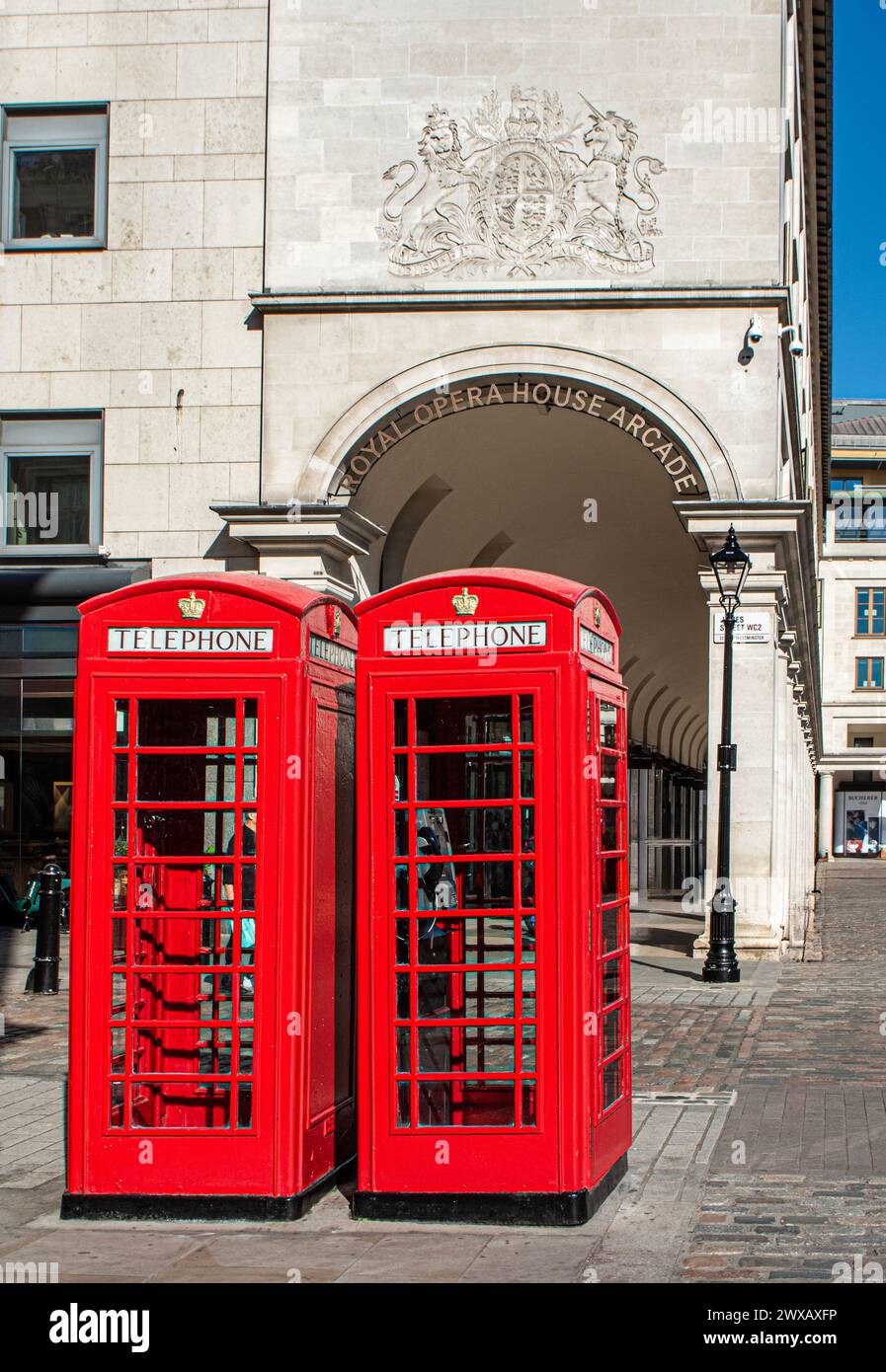 Rote Telefonzellen vor dem Eingang zur Royal Opera House Arcade mit dem Eingangsschild Covent Garden, London in der Sonne. Stockfoto