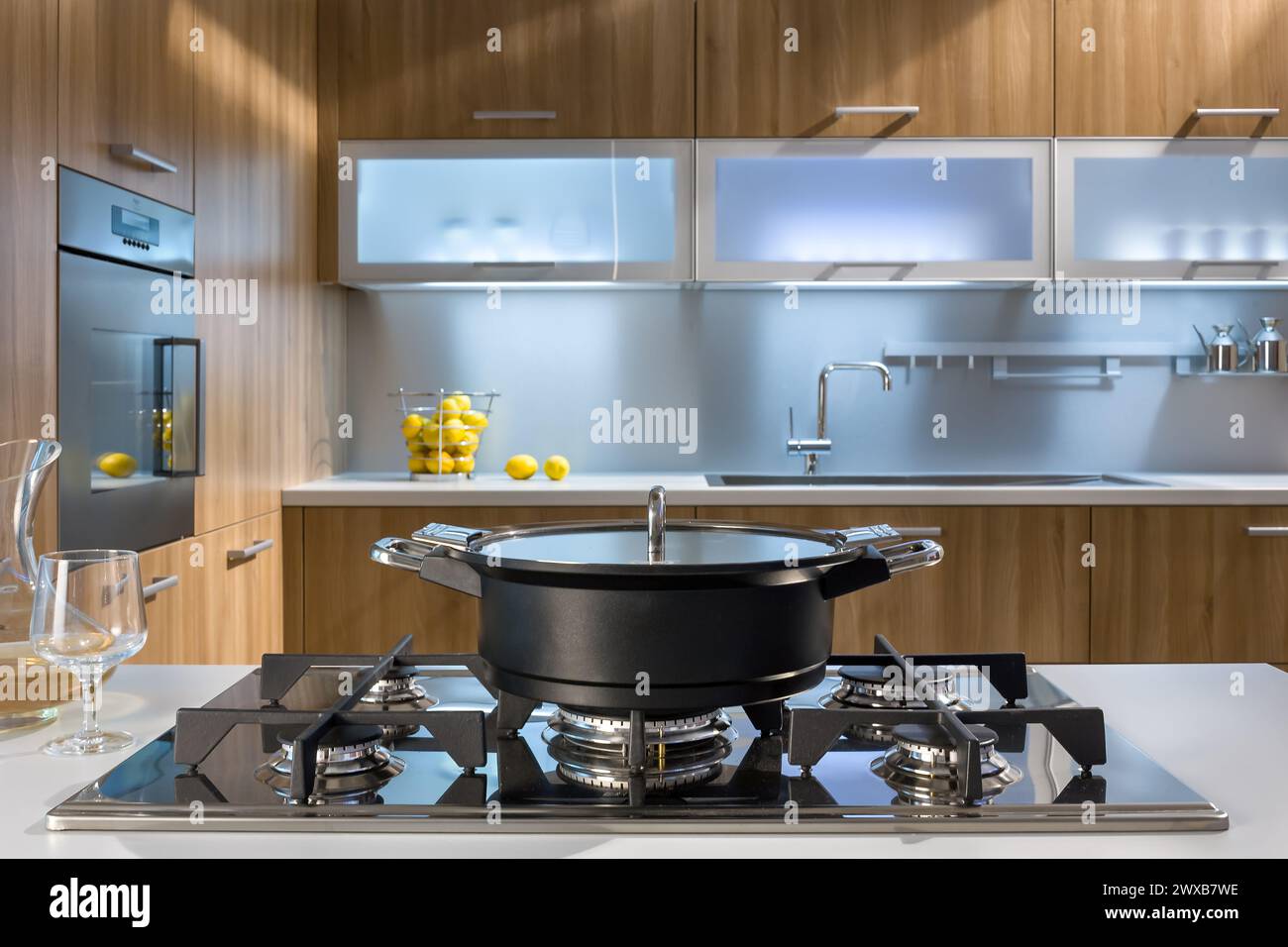Moderne Küche mit Gasherd, schwarzem Topf, Zitronen und Holzschränken. Das klare Design vereint Wärme, Eleganz und kulinarische Funktionalität. Stockfoto