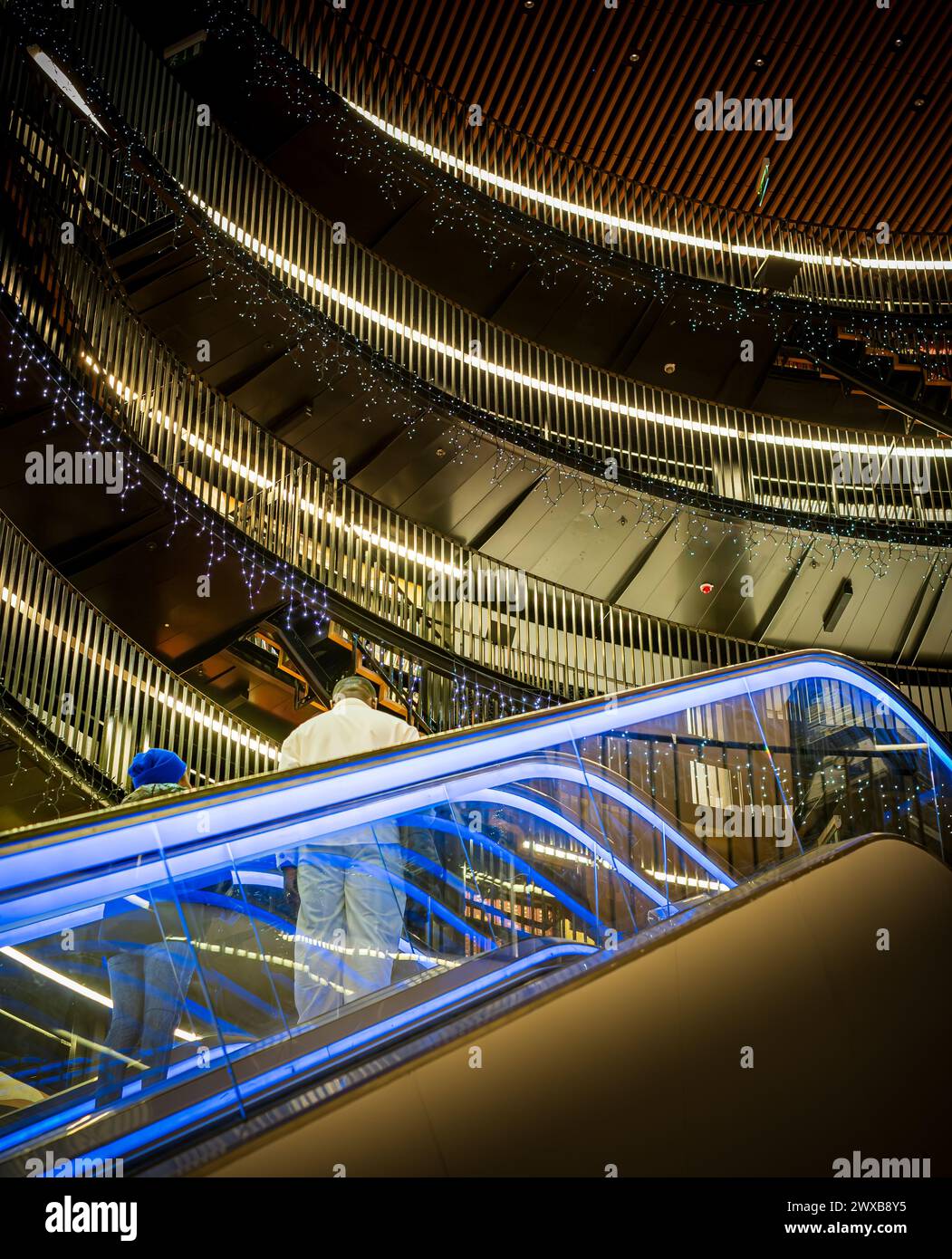 Blick nach oben auf das Innere der Birmingham City Library mit zwei Personen auf beleuchteter Rolltreppe und Bibliotheksgalerien darüber Stockfoto
