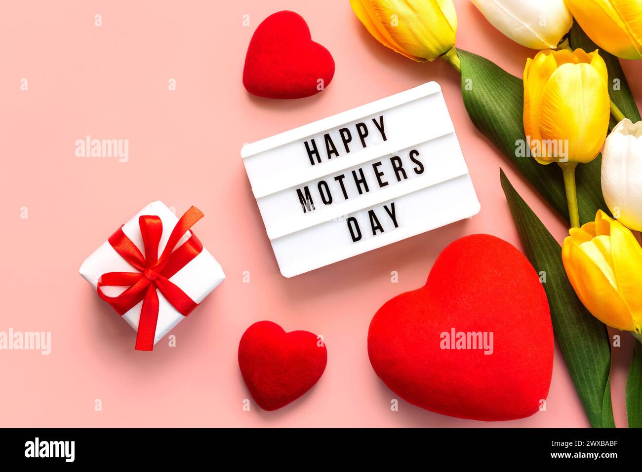 Alles Gute zum Muttertag. Leuchtkasten mit dem Wort Happy Mother's Day, Herzen und weißen und gelben Tulpen auf rosa Hintergrund. Muttertagskonzept Stockfoto