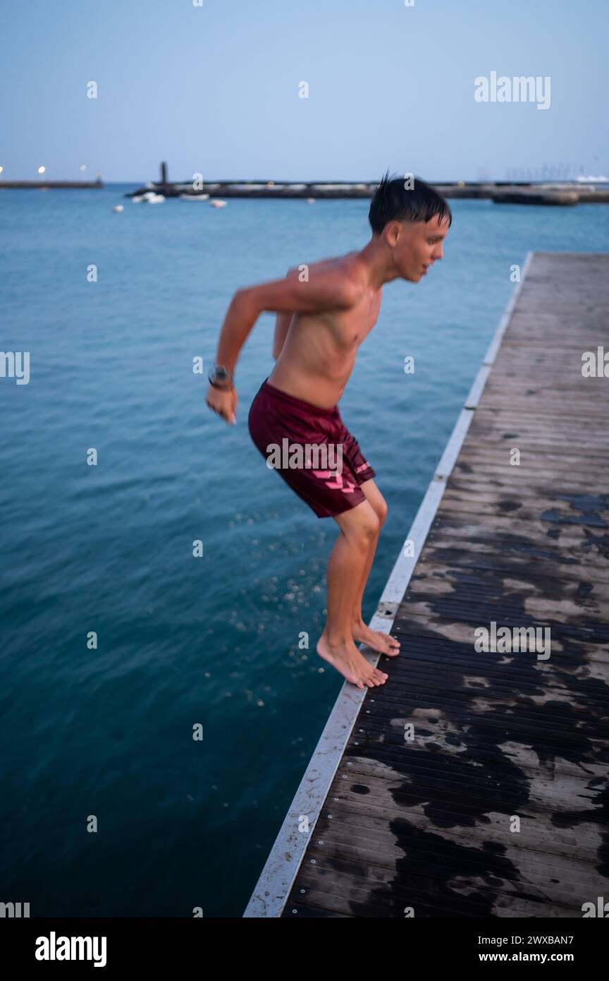 Teenager springen bei Sonnenuntergang von einem Dock in Arrecife, Lanzarote, Kanarischen Inseln, Spanien Stockfoto
