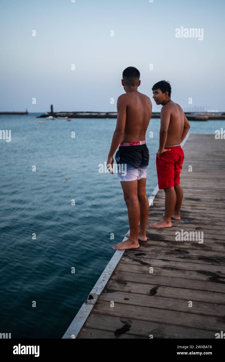Teenager springen bei Sonnenuntergang von einem Dock in Arrecife, Lanzarote, Kanarischen Inseln, Spanien Stockfoto