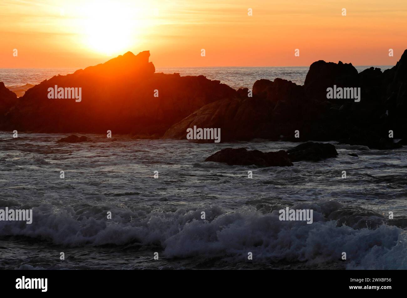 Die Silhouetten der Felsen stehen im Kontrast zu den Wellen des Meeres unter einem orangefarbenen Himmel bei Sonnenaufgang in der Nähe von Mindelo, Porto, Nordportugal, Portugal Stockfoto
