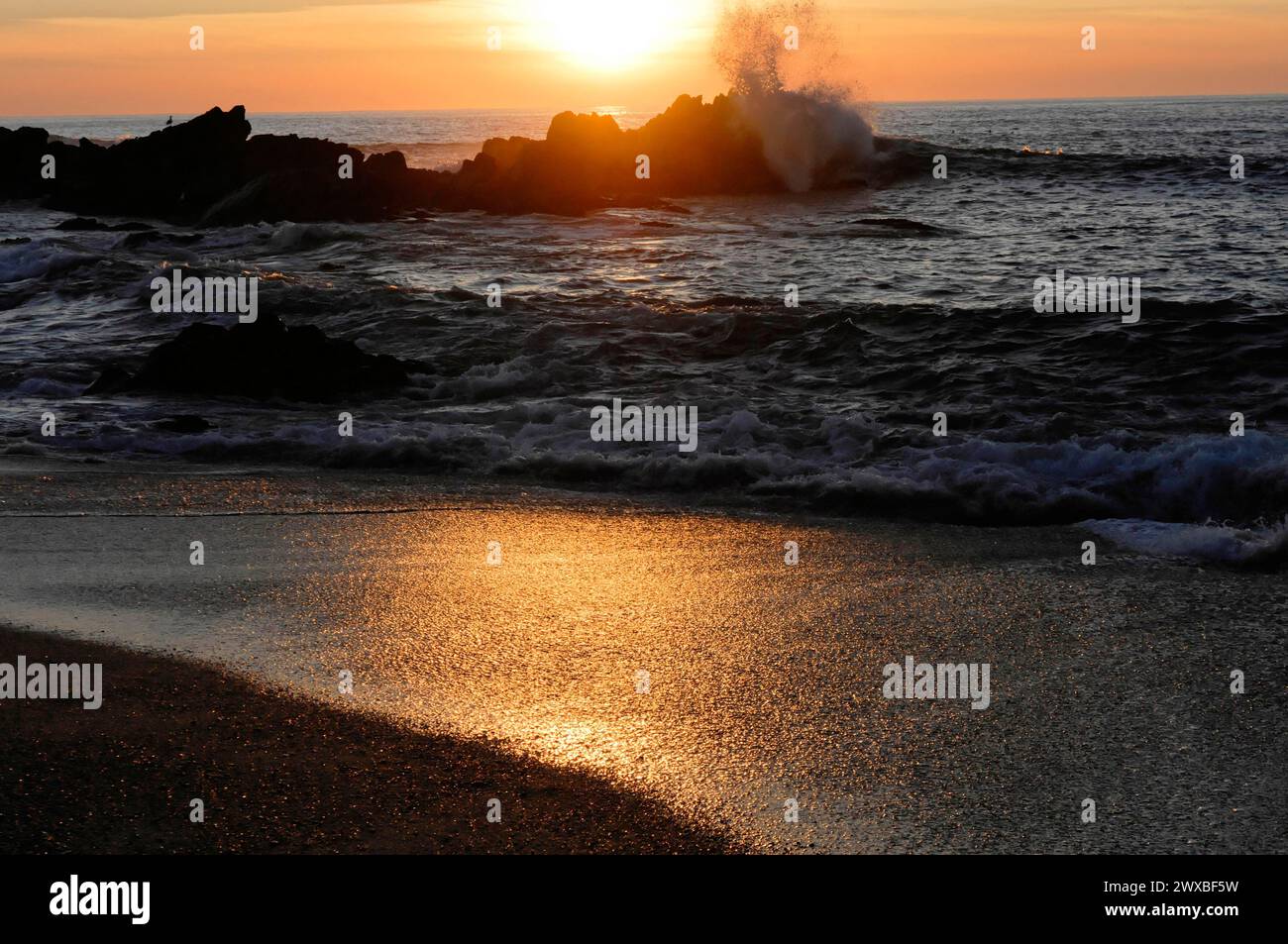 Wellen, die bei Sonnenuntergang gegen Felsen im Meer prallen und ein dynamisches und kraftvolles Bild schaffen, in der Nähe von Mindelo, Porto, Nordportugal, Portugal Stockfoto