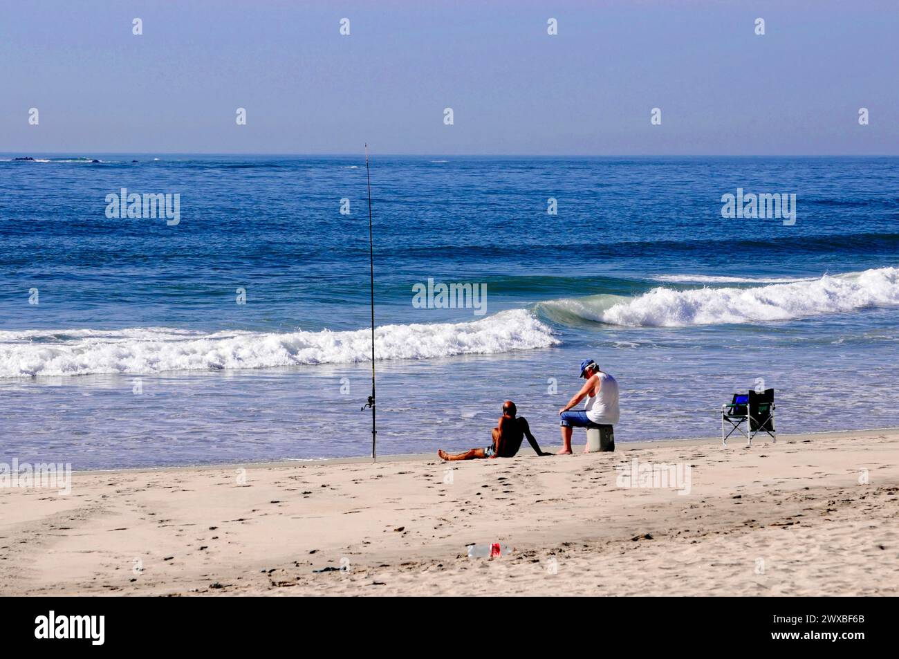 Zwei Leute entspannen am Strand, einer sitzt auf dem Sand, der andere steht, Meer im Hintergrund, in der Nähe von Mindelo, Nordportugal, Portugal Stockfoto