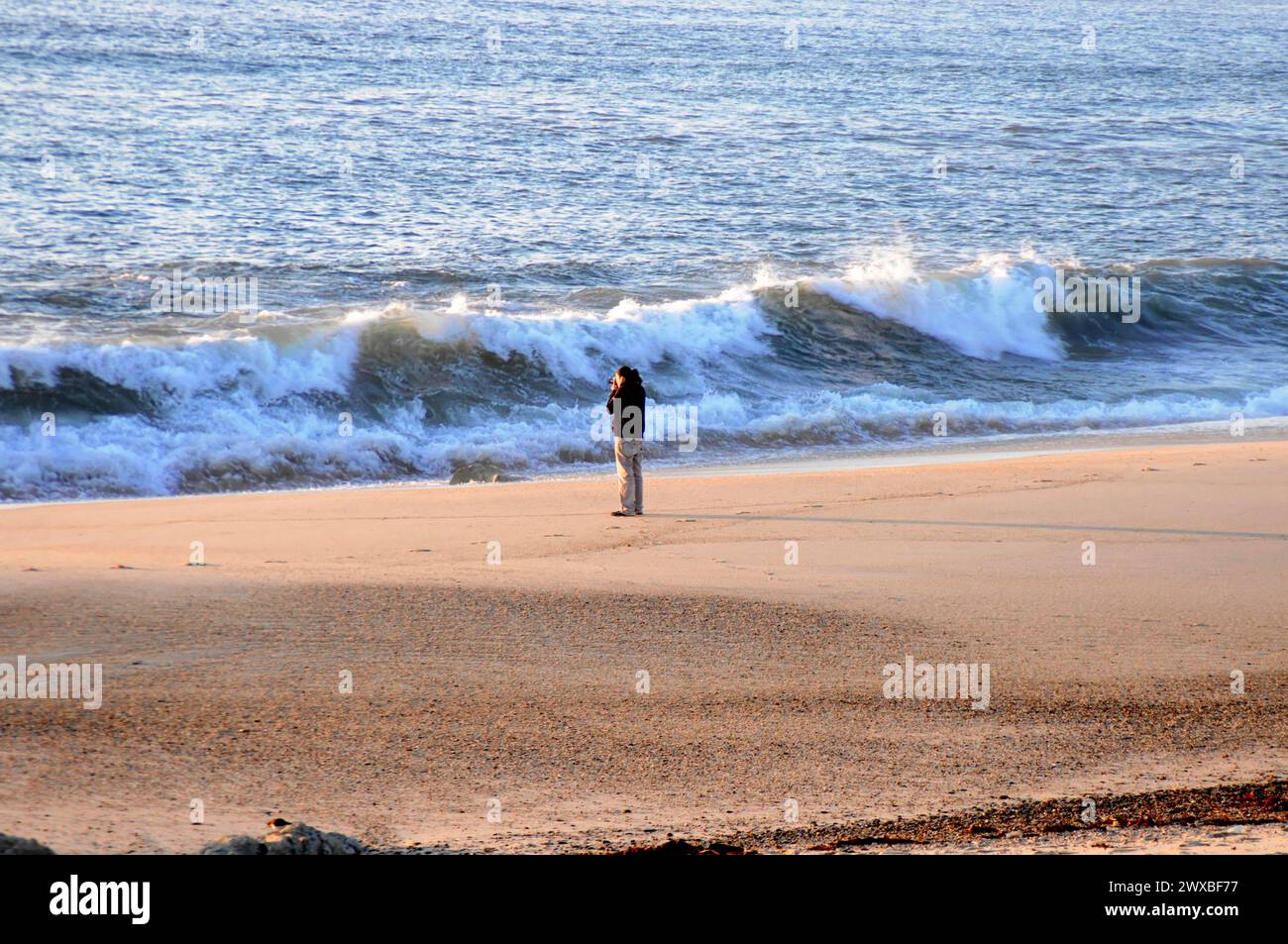 Eine Person steht allein am Strand mit Blick auf das Meer, umgeben von Wellen und Sand in der Dämmerung, in der Nähe von Mindelo, Porto, Nord-Portugal, Portugal Stockfoto