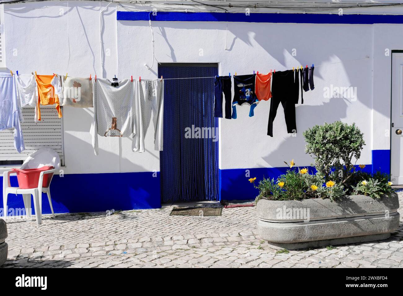 Nazare, Oeste, Bezirk Leiria, Weißes Haus mit bunten Kleidern auf einer Wäscheleine und Blumen in Töpfen, Nordportugal, Portugal Stockfoto