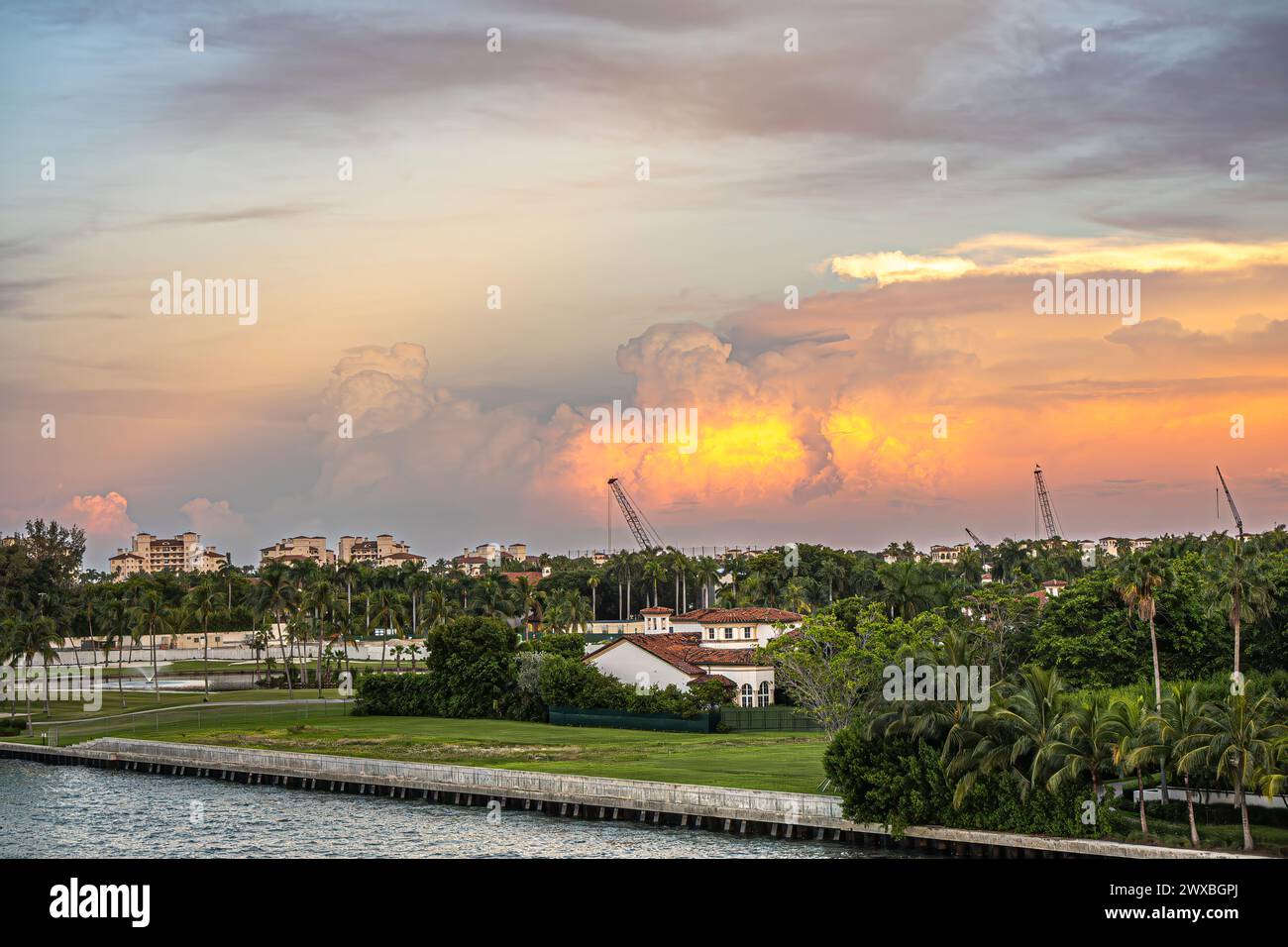 Miami, Florida, USA - 29. Juli 2023: Pilz-orange Sonnenuntergang Wolke über 6905 Herrenhaus Luxus entlang der Küste von Fisher Island N unter Abendhimmel. Grüner Rasen Stockfoto