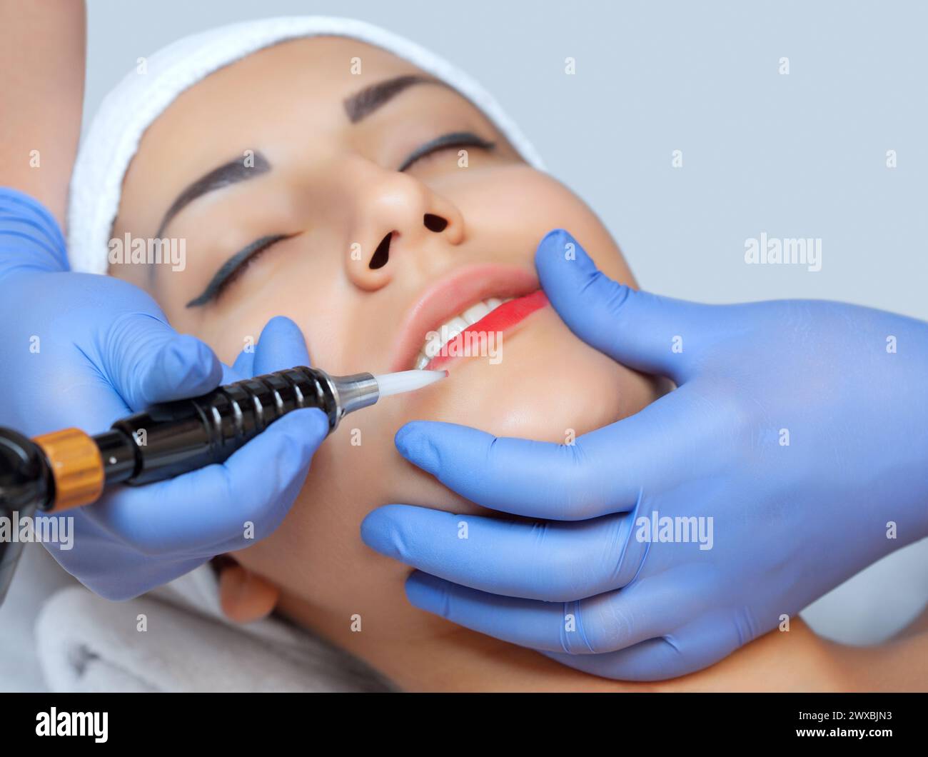 Permanentes Make-up für rote Lippen der schönen Frau im Schönheitssalon. Nahaufnahme-Kosmetikerin, die Lippen tätowiert. Stockfoto