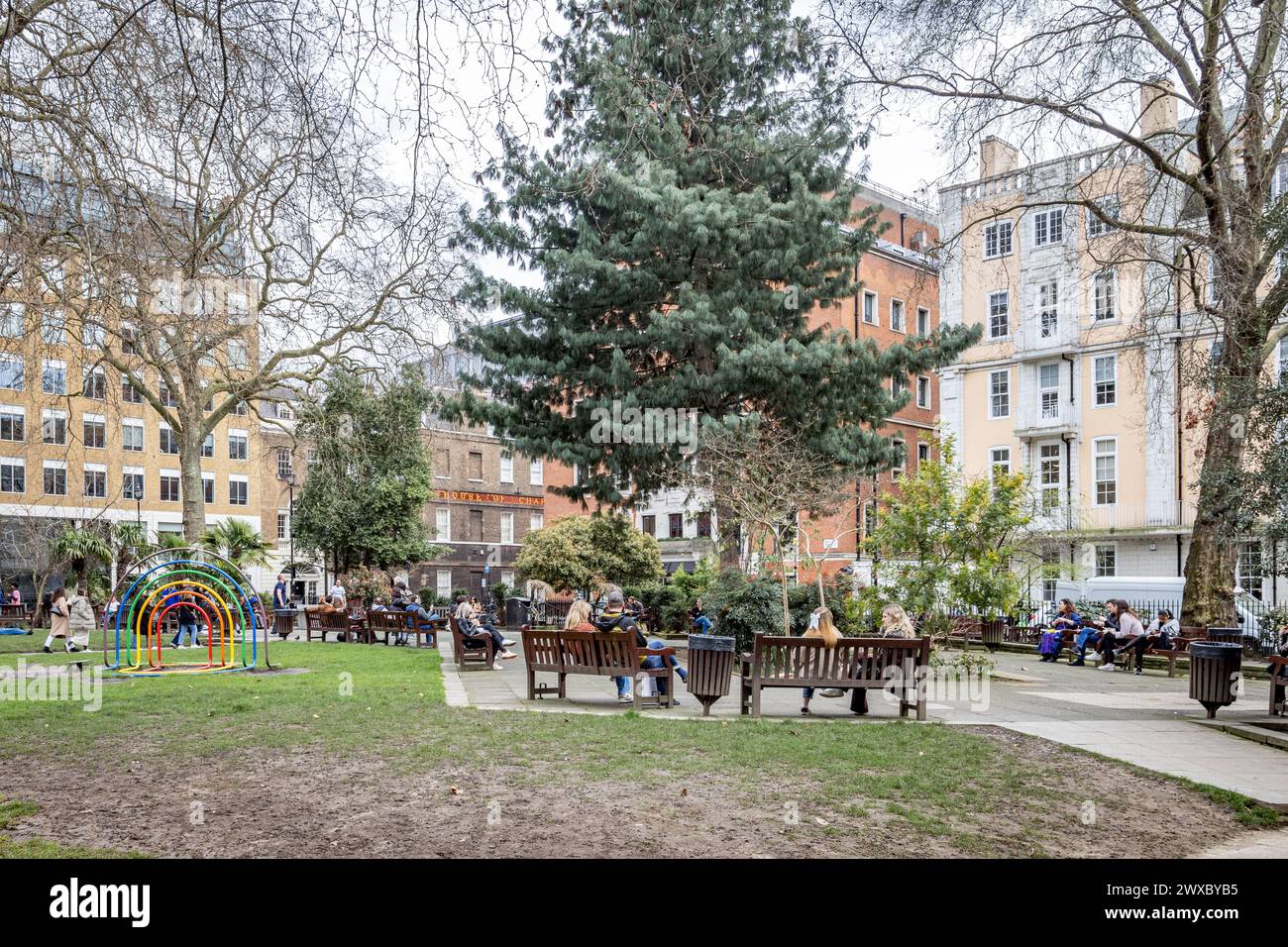 Leute, die sich unterhalten und ausruhen, während sie auf den Bänken in Soho Gardens, Soho Square, London sitzen. Stockfoto