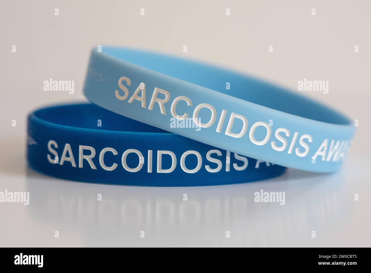 Zwei Sarkoidose Awareness Armbänder, dunkelblau und blassblau auf weißem Hintergrund. Stockfoto