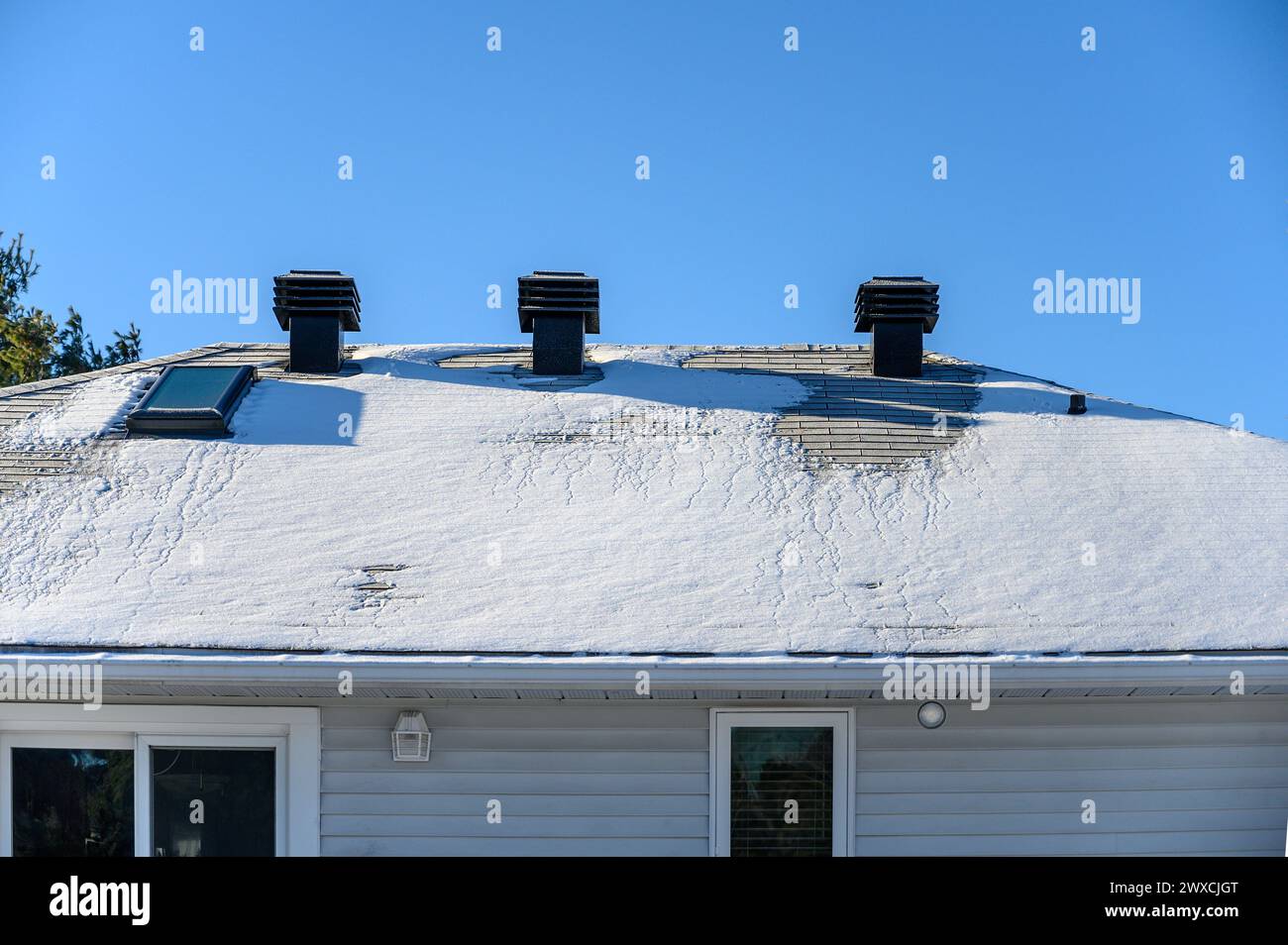 Drei Lüftungsschlitze auf dem Dach und ein Oberlicht auf einem teilweise schneebedeckten Dach Stockfoto