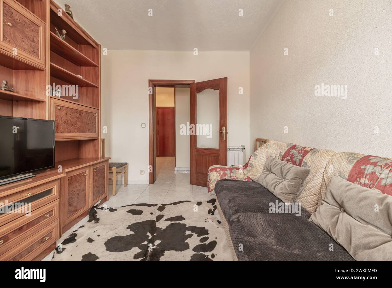 Wohnzimmer eines Hauses mit Stoffsofas in alten und schmutzigen Farben, einem Bücherregal aus imitiertem Wurzelholz und einem mit synthetischem Rindleder bedeckten Boden Stockfoto