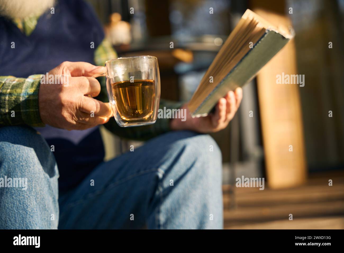 Ein älterer Mann sitzt mit einem Buch auf der Veranda Stockfoto