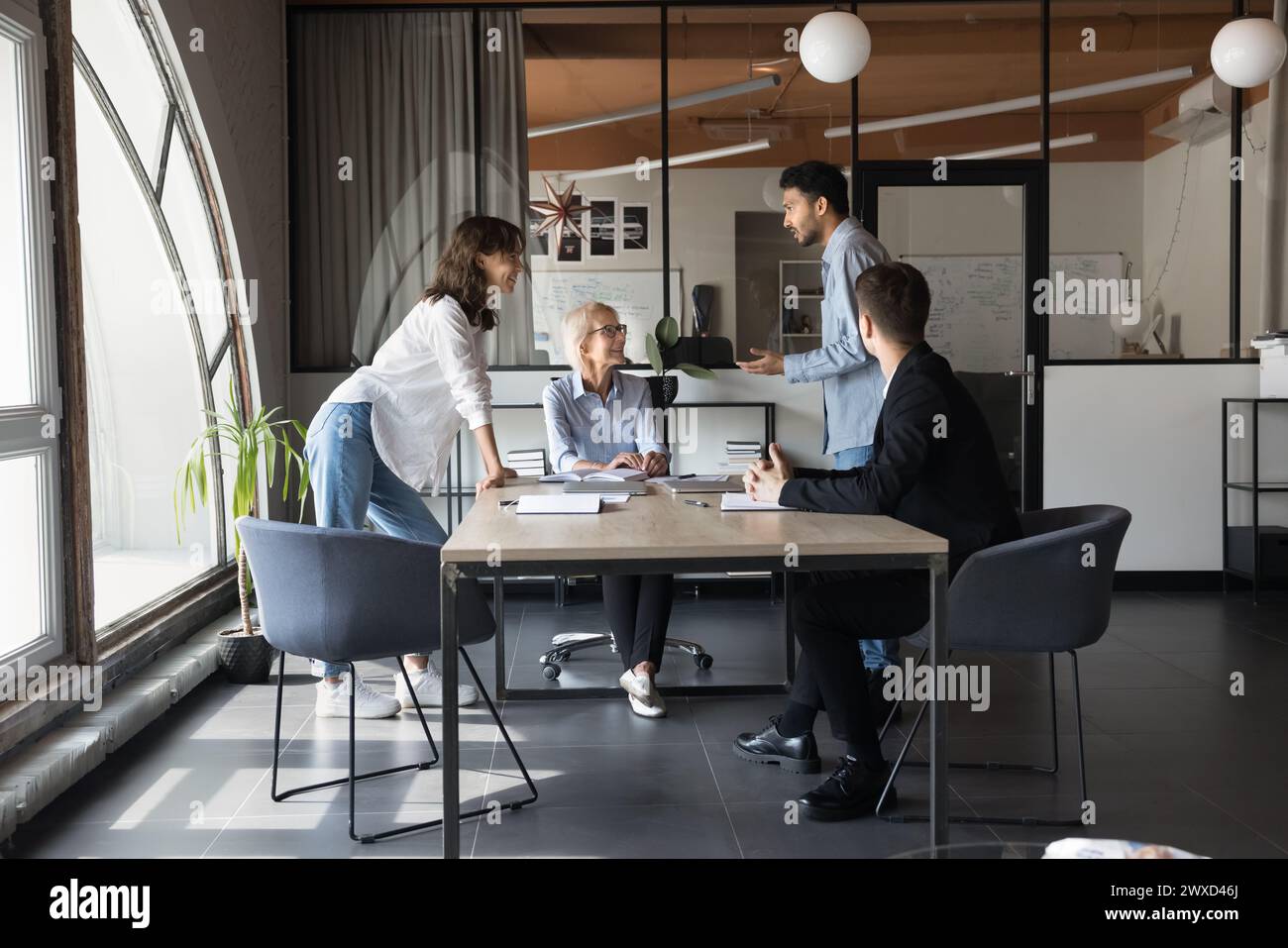Happy inspirierte jüngere und ältere Kollegen, die sich bei einem Meeting unterhalten Stockfoto
