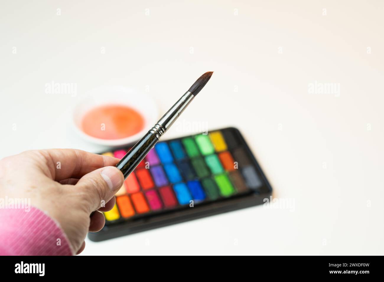 Eine Hand hält einen nassen Pinsel auf einem warmen Aquarellset. Stockfoto