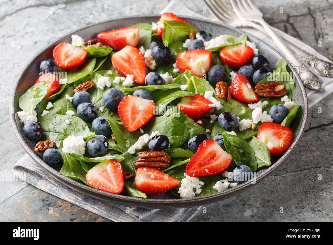 Spinatsalat mit Erdbeeren, Heidelbeeren, Käse und Pekannüssen mit Honigdressing in Nahaufnahme auf einem Teller auf dem Tisch. Horizontal Stockfoto