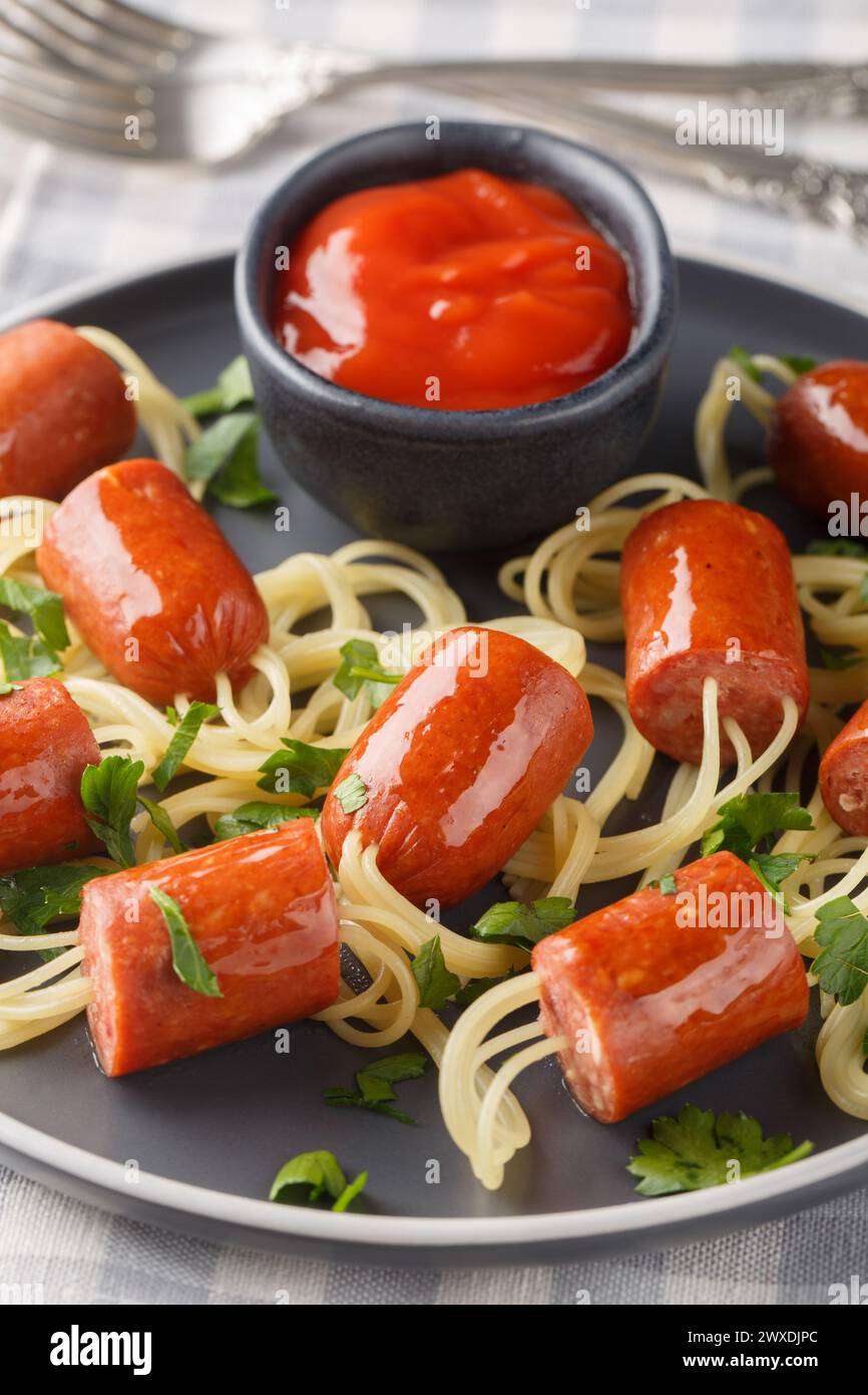 Festliche lustige Essensspaghetti mit Würstchen und Ketchup Nahaufnahme auf einem Teller auf dem Tisch. Vertikal Stockfoto