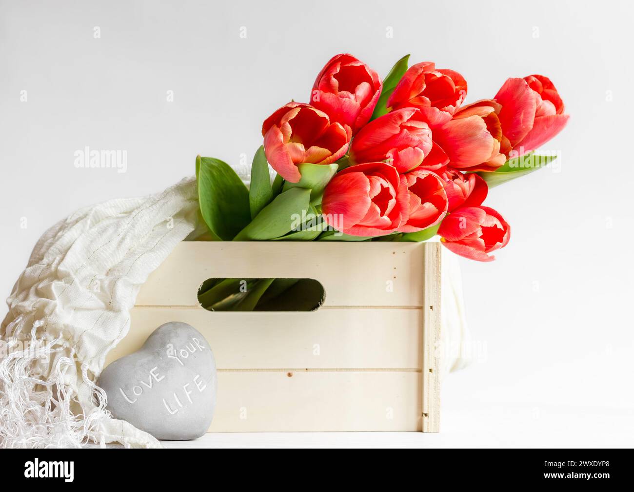 Rote Tulpen in einer Holzkiste mit einem Kieselstein, auf dem "Liebe dein Leben" steht Stockfoto
