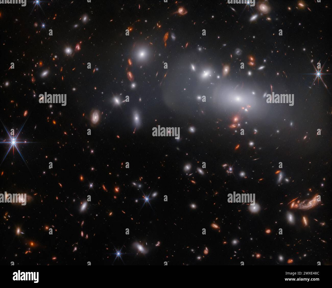 Diese Beobachtung des James Webb Space Telescope zeigt den massereichen Galaxienhaufen RX J2129, der etwa 3,2 Milliarden Lichtjahre von der Erde entfernt im Sternbild Aquarius liegt. Gravitationslinsen können dazu führen, dass Hintergrundobjekte seltsam verzerrt erscheinen, wie die konzentrischen Lichtbögen oben rechts in diesem Bild zeigen. Gravitationslinsen können nicht nur die Bilder von Hintergrundobjekten verzerren, sondern auch dazu führen, dass entfernte Objekte viel heller erscheinen als sonst. KREDIT: NASA/ESA/CSA Stockfoto
