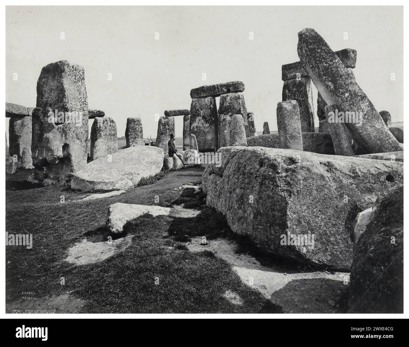 Ein unbekannter Mann sitzt auf einem Stein in Stonehenge. Schwarzweißfoto des Fotografen Francis Frith. 1864 - 1898. Stonehenge ist ein prähistorisches Denkmal auf der Salisbury Plain in Wiltshire, England, drei Meilen westlich von Amesbury. Sie besteht aus einem äußeren Ring aus vertikalen Sarsensteinen, die jeweils etwa 13 Fuß hoch, sieben Fuß breit und etwa 25 Tonnen schwer sind, gekrönt von horizontalen Sturzsteinen aus dem Bronzezeitalter Großbritannien Stockfoto