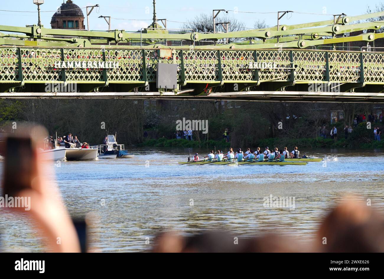 Die Teams aus Cambridge und Oxford passieren die Hammersmith Bridge während des 169. Men's Gemini Boat Race 2024 auf der Themse, London. Bilddatum: Samstag, 30. März 2024. Stockfoto
