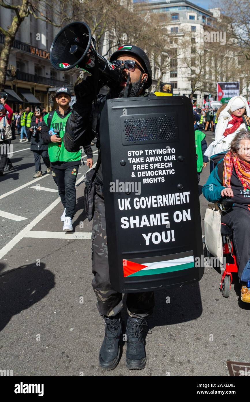 The Strand, London, Großbritannien. 30. März 2024. Während der Konflikt zwischen Israel und der Hamas anhält, findet ein Protest gegen die Eskalation der militärischen Aktionen im Gazastreifen statt. Organisiert von Gruppen wie der palästinensischen Solidaritätskampagne und der „Stop the war Coalition“ mit dem Titel „nationale Demonstration“ und mit Aufrufen zu „Stop the Genocide“, „Ceasefire Now“ und „Free Palestine“, brachen die Demonstranten vom Russell Square auf, bevor sie zum Trafalgar Square fuhren. Männlich in paramilitärischer Uniform mit Megaphon. FOA Stockfoto