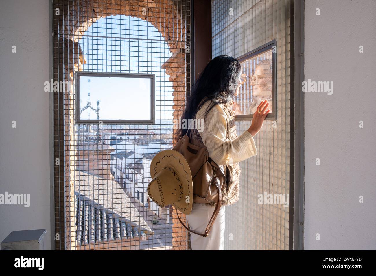 Eine Frau mittleren Alters mit Hut blickt aus dem Turm der Kirche San Agustin in Almagro, Ciudad Real, Spanien. Die Aussicht vom Turm ist o Stockfoto
