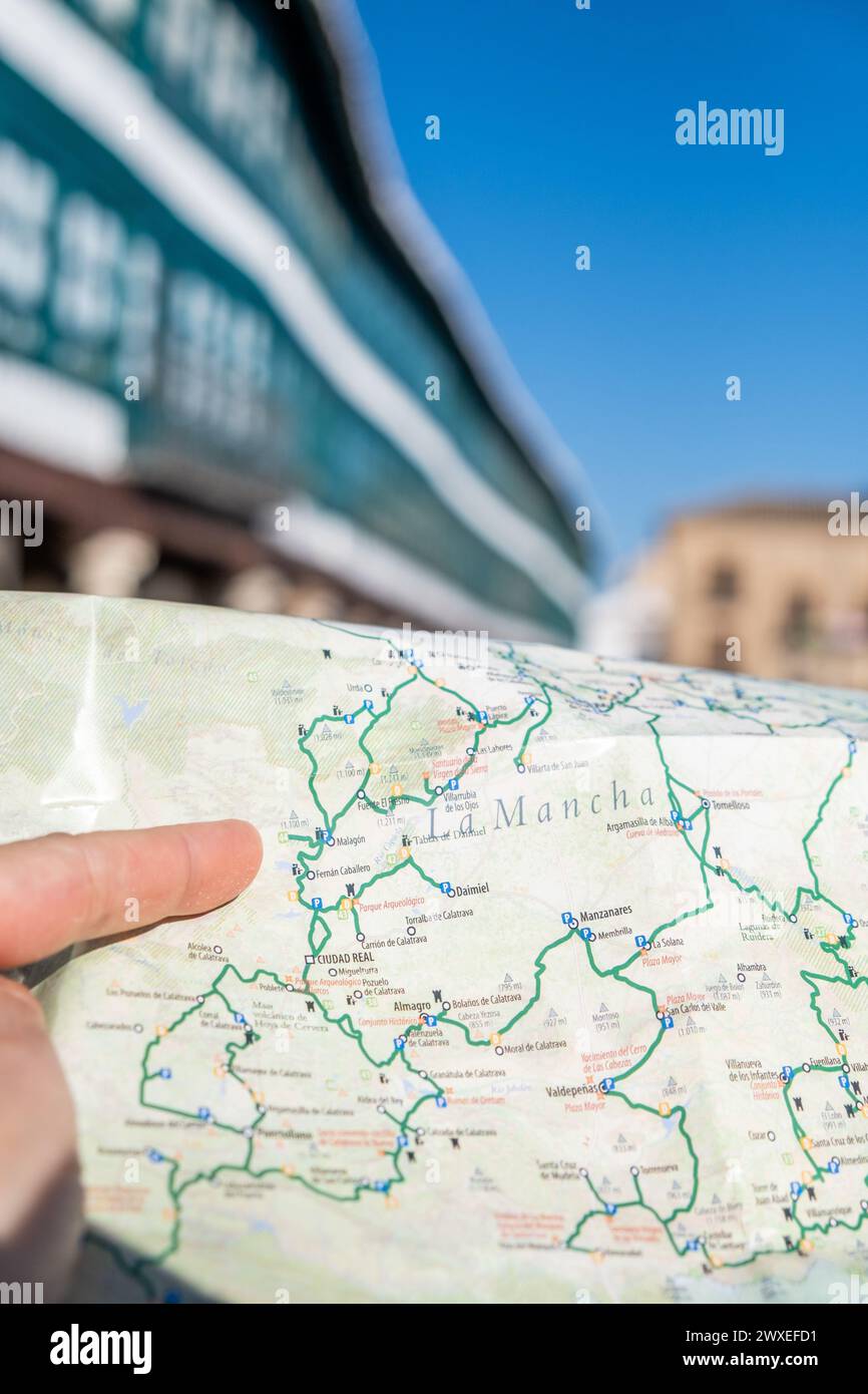 Finger signiert ein Detail einer Touristenkarte von Castilla la Mancha, Spanien, mit dem Hauptplatz von Almagro im Hintergrund, der an einem sonnigen Tag außer Fokus steht. It Stockfoto