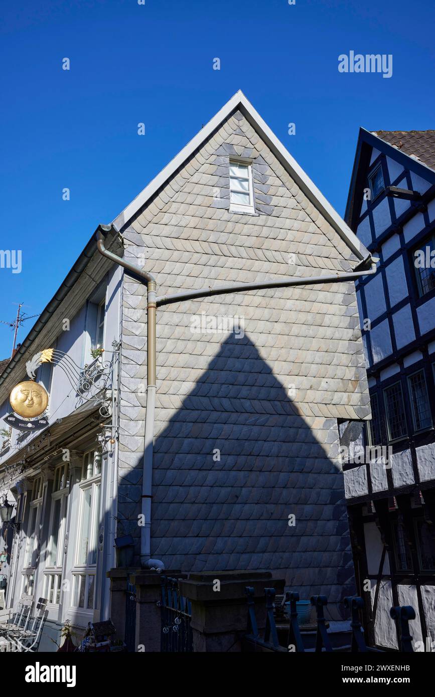 Schmales, schiefergetäfeltes Haus mit spitzem Dach und Schatten vor wolkenlosem blauem Himmel auf dem Kirchplatz in der Altstadt von Hattingen Stockfoto