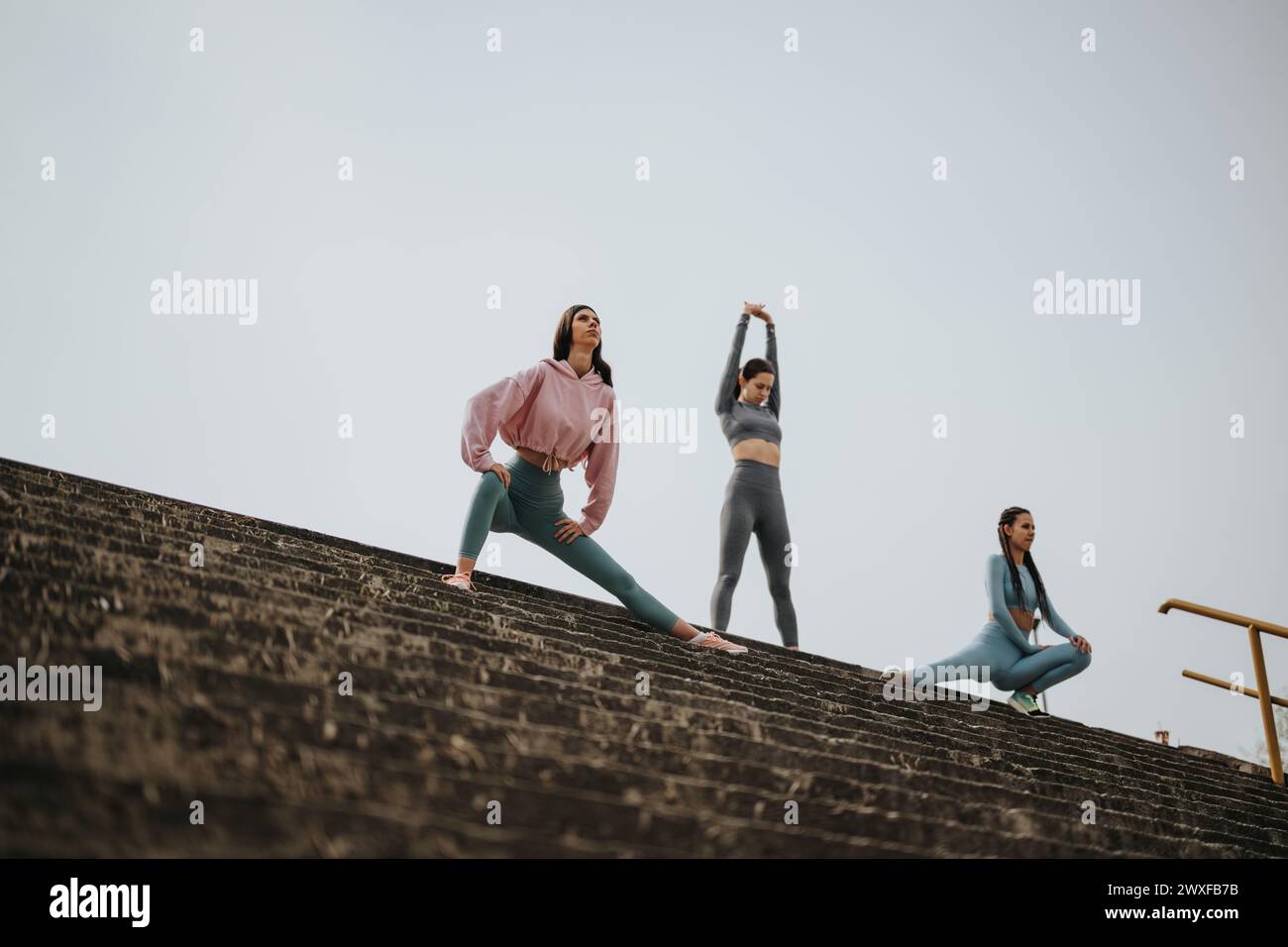 Frauen, die Dehnungsübungen im Freien auf Treppen durchführen und sich dabei auf Fitnessziele konzentrieren Stockfoto