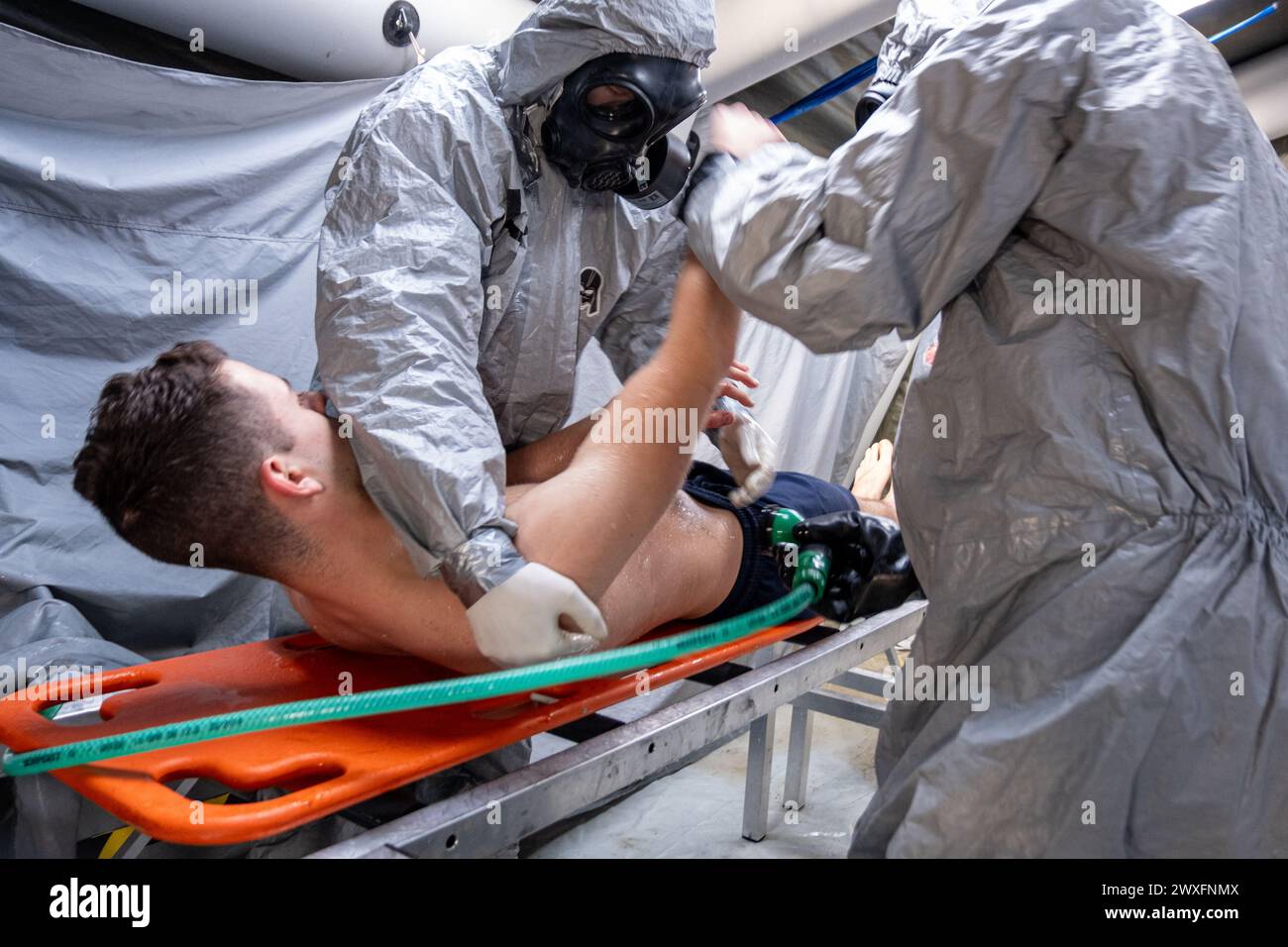Ein Mann in einem Krankenhausbett wird von zwei Männern in Gefahrenanzügen behandelt. Die Szene ist angespannt und ernst, da die Männer Schutzkleidung tragen und arbeiten Stockfoto