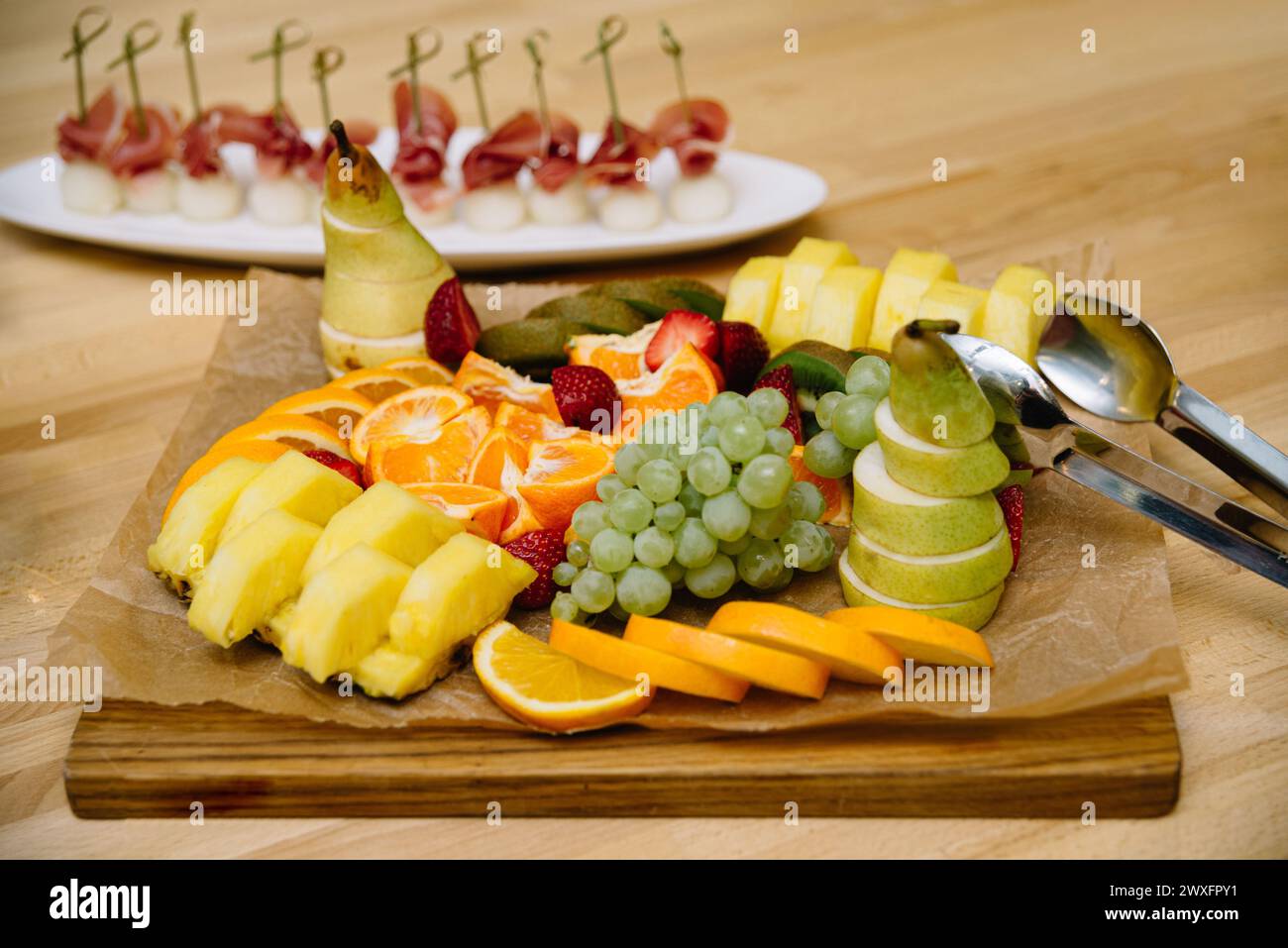 Eine bunte Präsentation von geschnittenem frischem Obst auf einem rustikalen Holzbrett, perfekt für einen gesunden Party-Snack oder ein Dessert Stockfoto