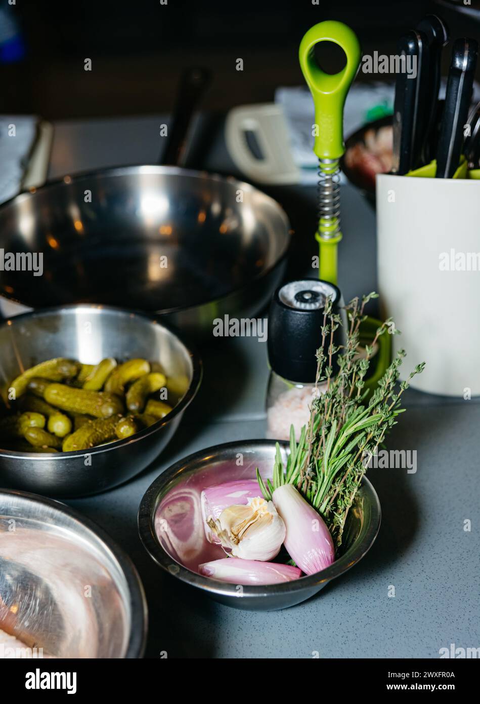 Kochbereich mit frischen Schalotten, Knoblauch und Thymian in Edelstahlschalen sowie Küchenutensilien. Stockfoto