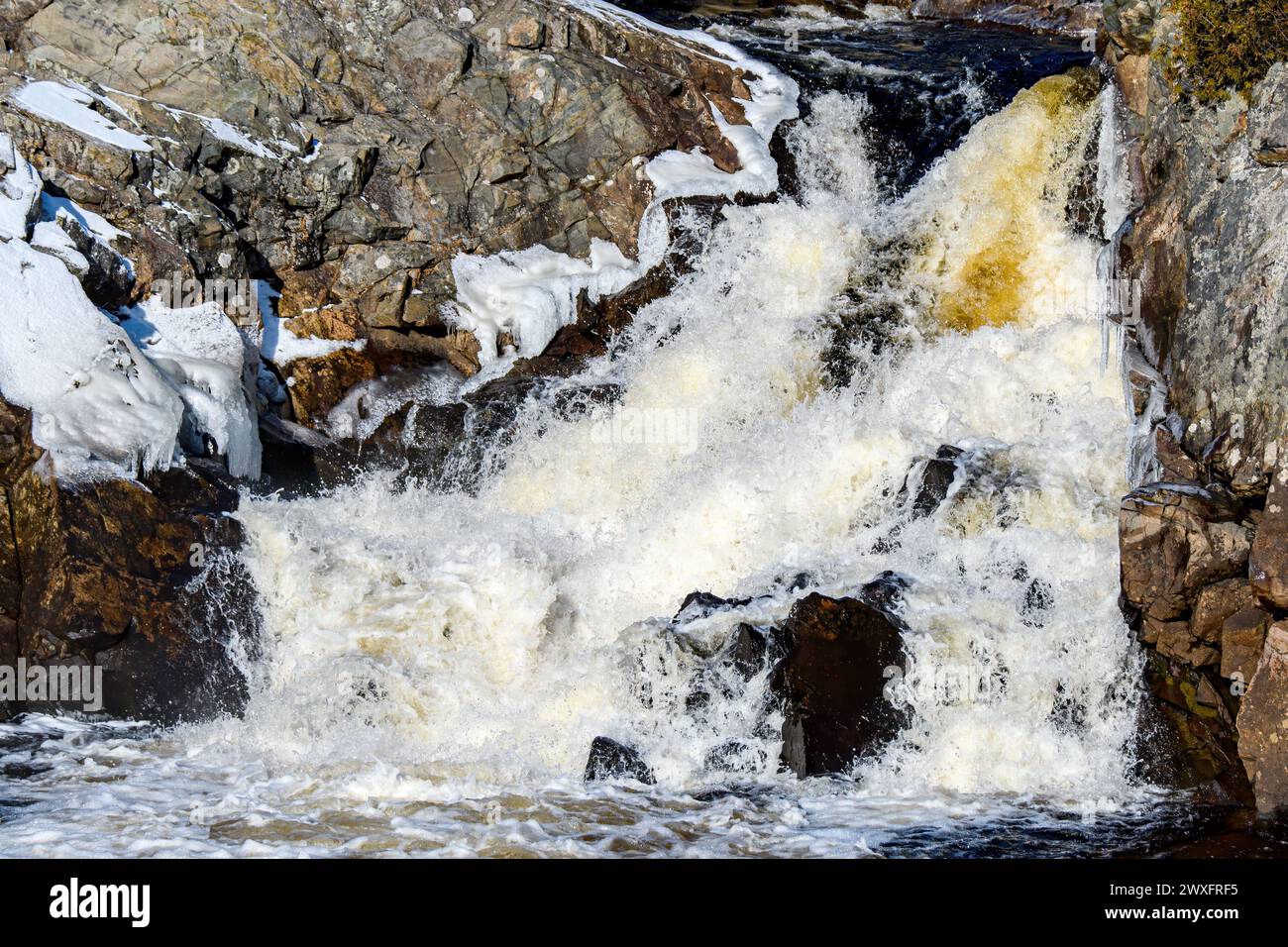 Ein kleiner, schnell fließender Wasserfall im Winter. Um den Wasserfall herum ist etwas Eis. Schnellverschluss zum Einfrieren der Action. Stockfoto