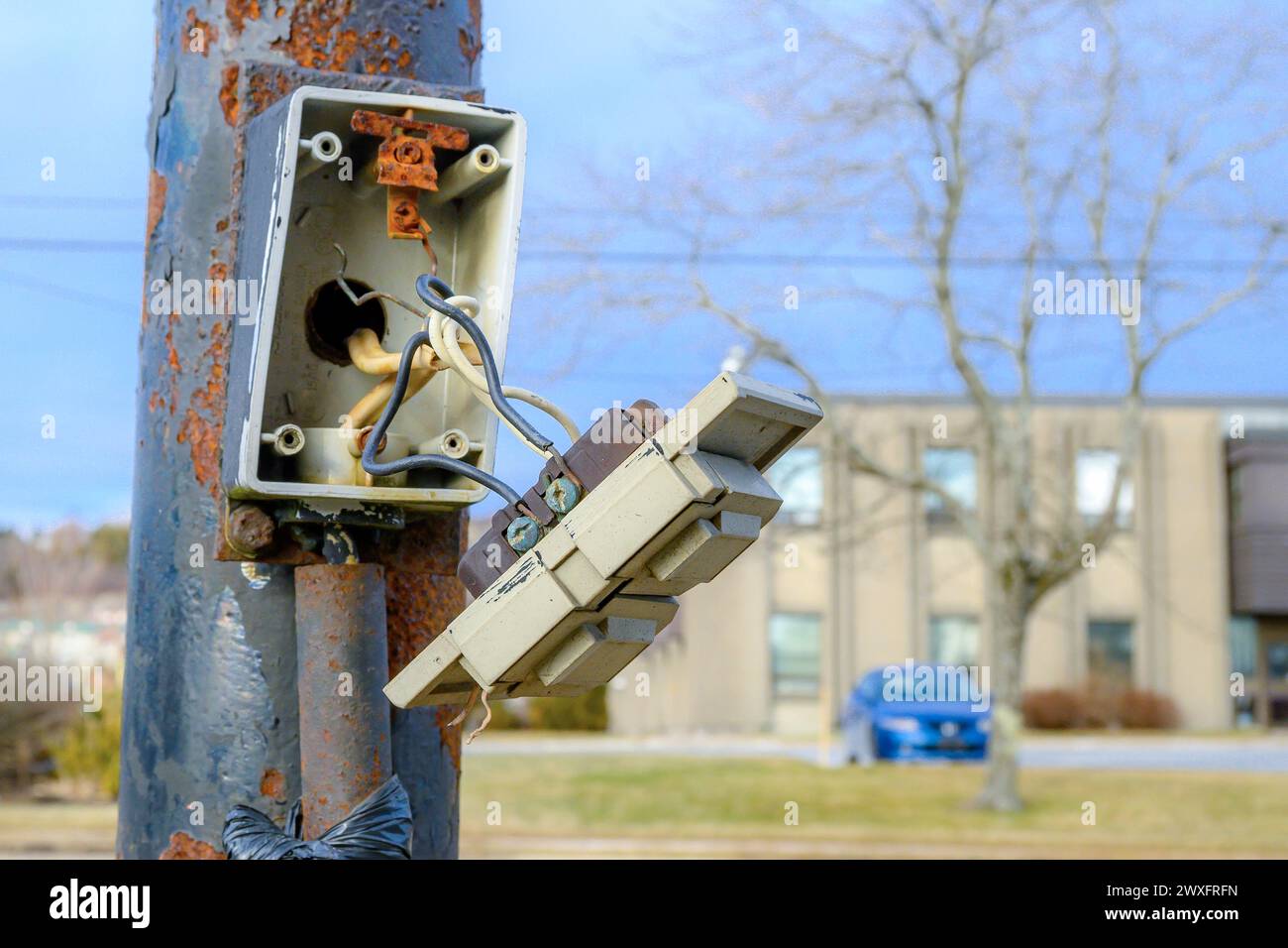Eine defekte elektrische Tafel an der Seite eines Außenmasts. Die Vorderseite hängt ab und wird nur von freiliegenden Drähten an der Box gehalten. Nahansicht. Stockfoto