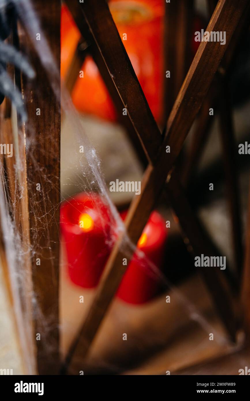 Eine stimmungsvolle Halloween-Szene mit roten Kerzen hinter Spinnweben, die eine geheimnisvolle und gruselige Atmosphäre in einer dunklen Umgebung schafft. Stockfoto