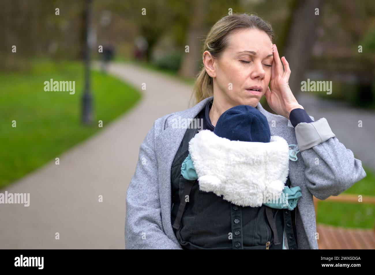 Erschöpfte und gestresste Frau, die ihr Baby in einer Babytrage im Park hält und trägt Stockfoto