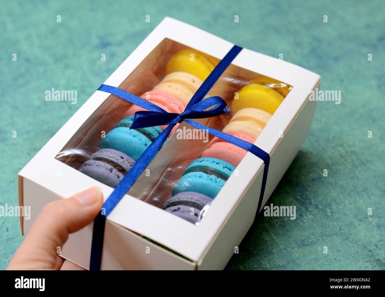 Farbenfrohe Auswahl an Macarons in einer Box, gebunden mit einem blauen Band, mit einer Vielzahl von delikaten und lebhaften französischen Backwaren Stockfoto