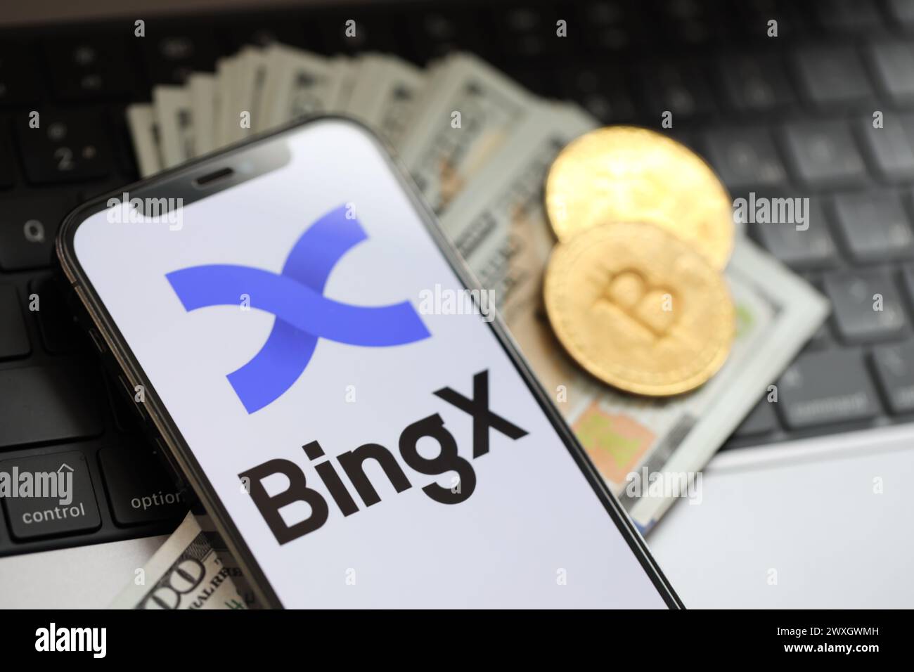 KIEW, UKRAINE - 15. MÄRZ 2024 BingX-Logo auf dem iPhone-Display mit Dollars und Bitcoins auf dem MacBook. Portal für den Austausch von Kryptowährungen Stockfoto