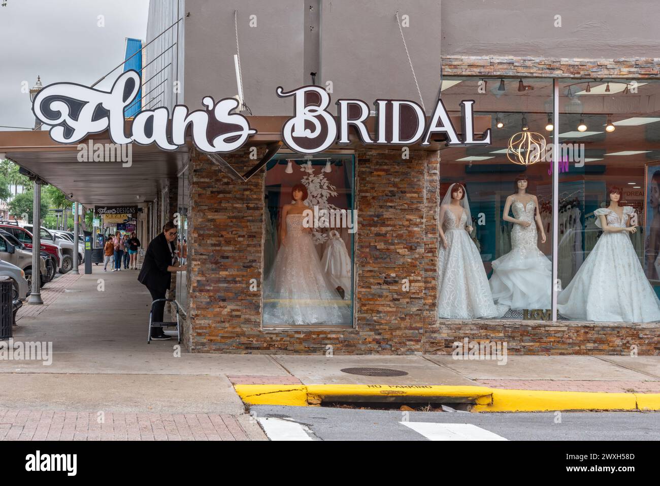 Außenansicht von Flan's Bridal Shop mit Schaufensterpuppen in weißen Brautkleidern im Zentrum von McAllen, Hidalgo County, Texas, USA. Eine Frau wäscht die Fenster. Stockfoto